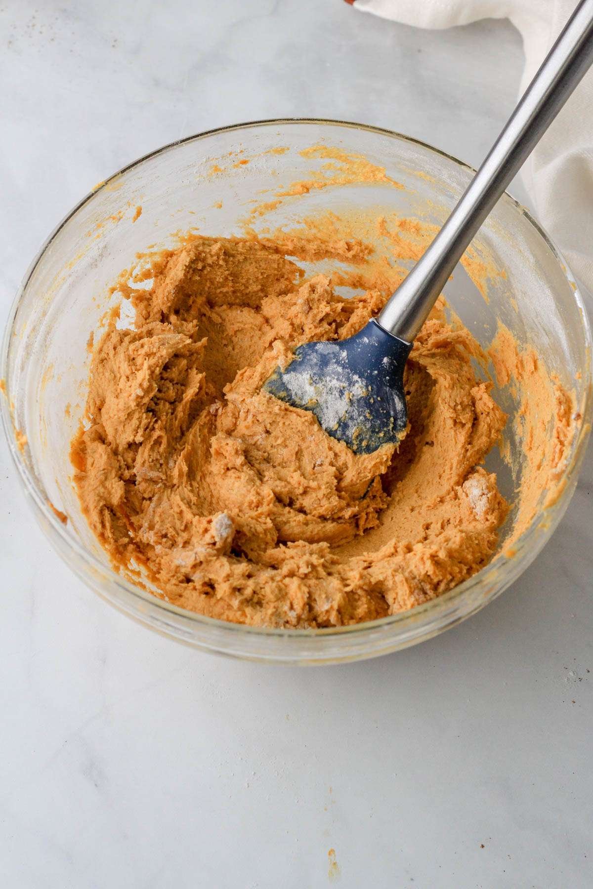 A glass bowl with dairy-free pumpkin spice cookie dough and a blue spatula after folding in the dry ingredients.