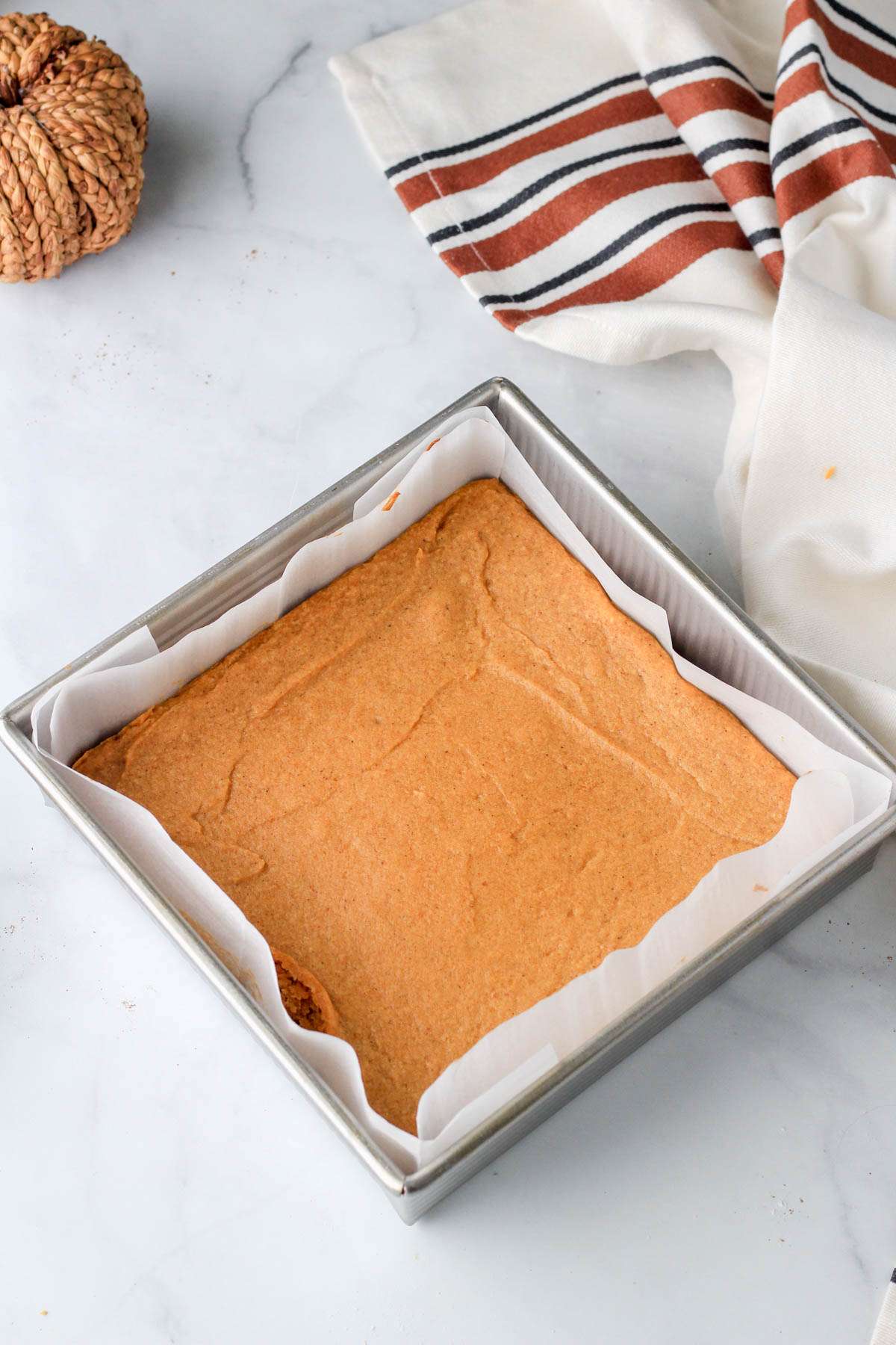 A square silver baking pan lined with parchment paper after baking pumpkin spice cookie bars.