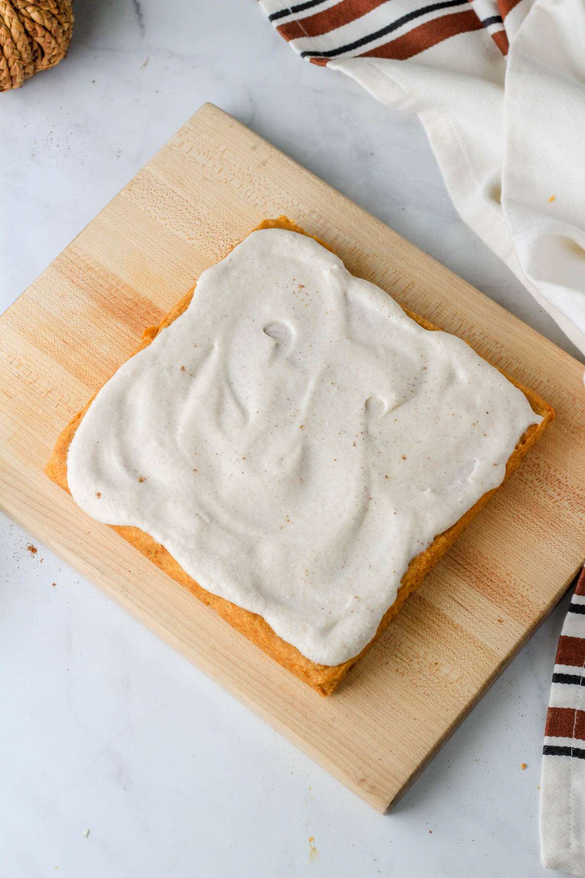 A wooden cutting board with pumpkin spice cookie bars topped with pumpkin spice buttercream and sprinkled with pumpkin spice seasoning.