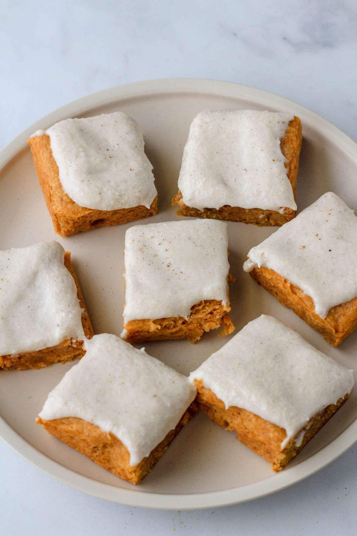 A white plate with seven squares of dairy-free pumpkin spice cookie bars topped with pumpkin spice buttercream.