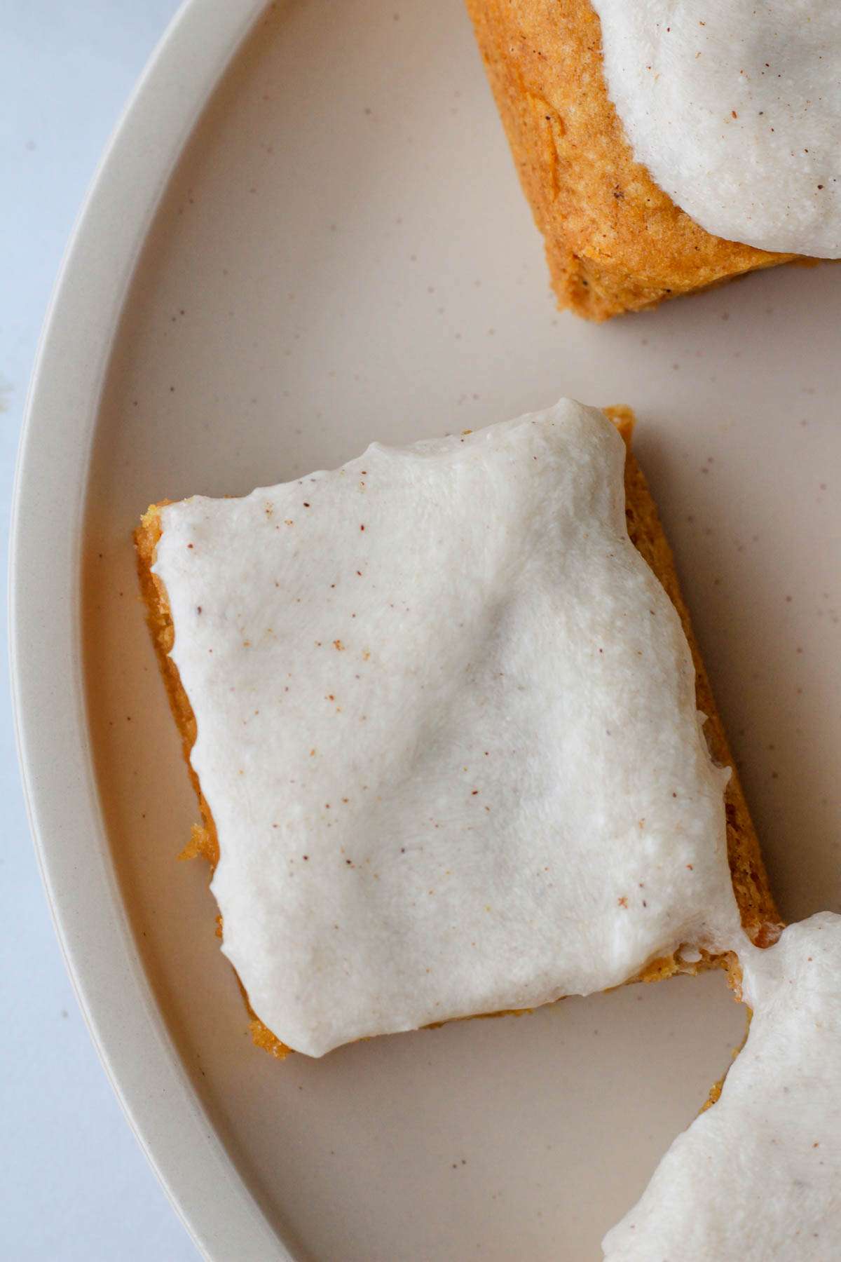 A white plate with a cookie bar on it topped with pumpkin spice buttercream.