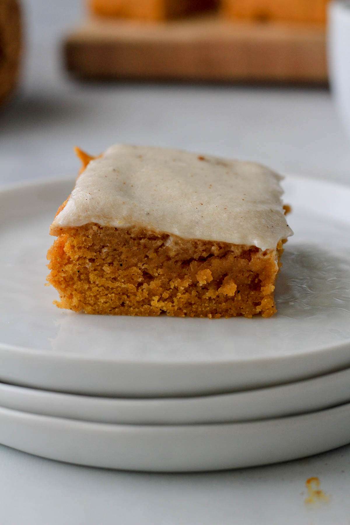 A stack of white plated and one pumpkin spice cookie bar topped with dairy-free pumpkin spice buttercream.
