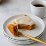 A fork with a bite of pumpkin spice cookie bar on a stack of white plates in front of a small cup of coffee.