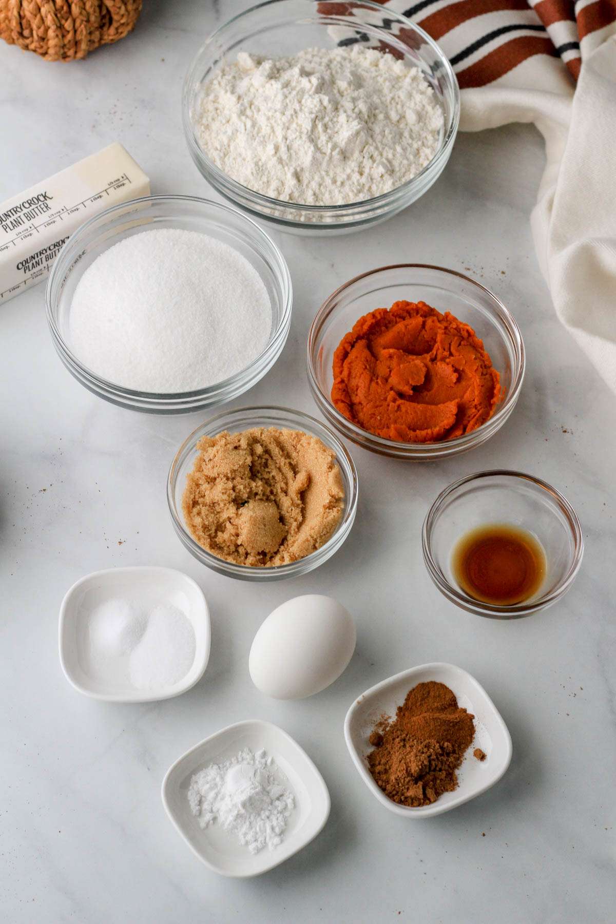 Ingredients for pumpkin spice cookie bard on a white counter with a small woven pumpkin in the back.