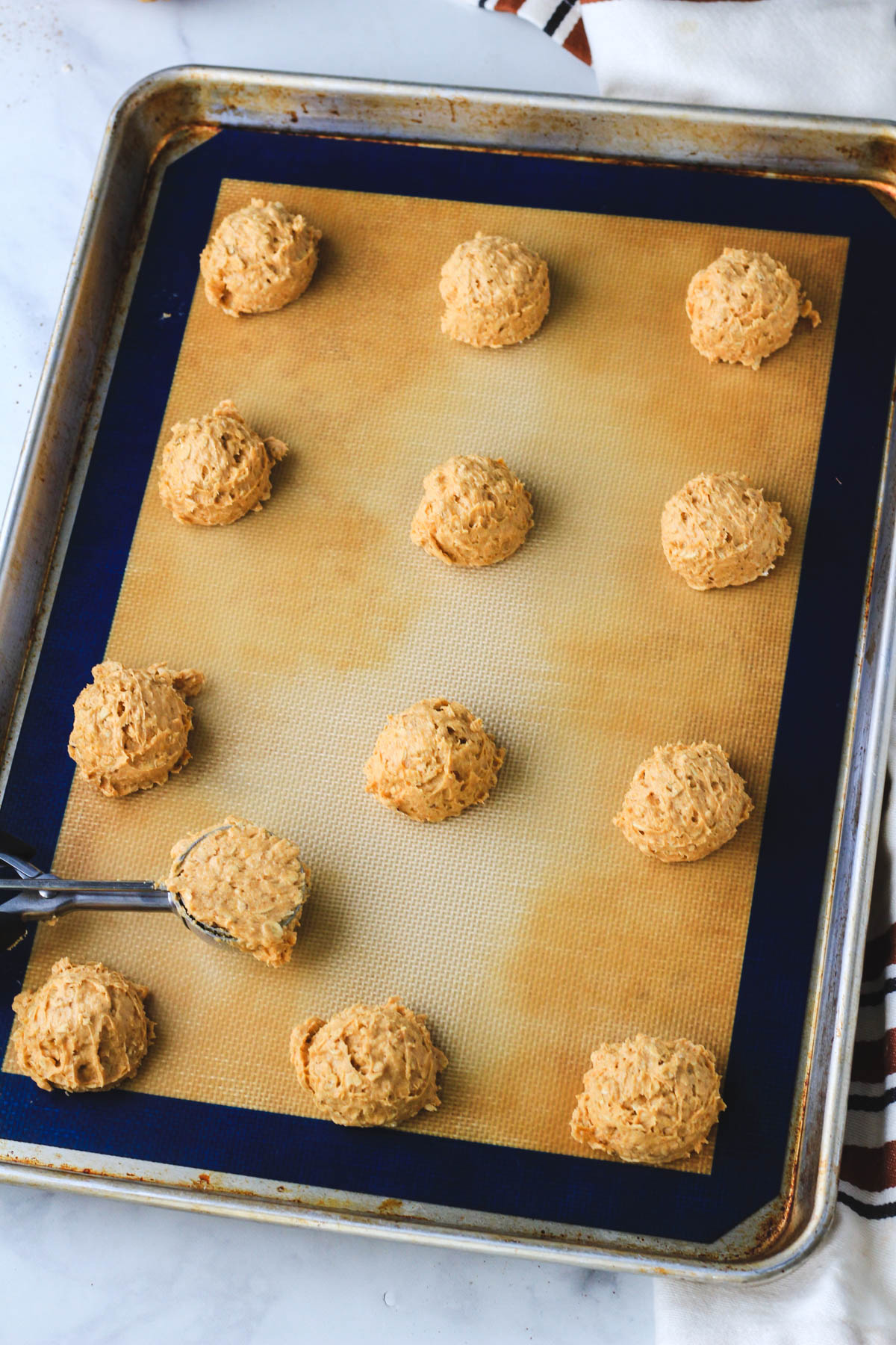 A rimmed cookie sheet lined with a silicone baking mat and cookie dough before baking.