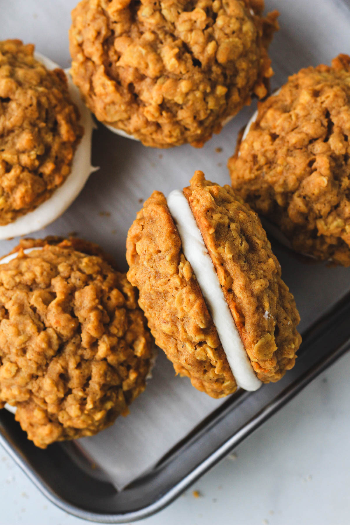 A small rimmed cookie sheet with pumpkin spice oatmeal cream pie cookies with one turned on the side to see the filling.