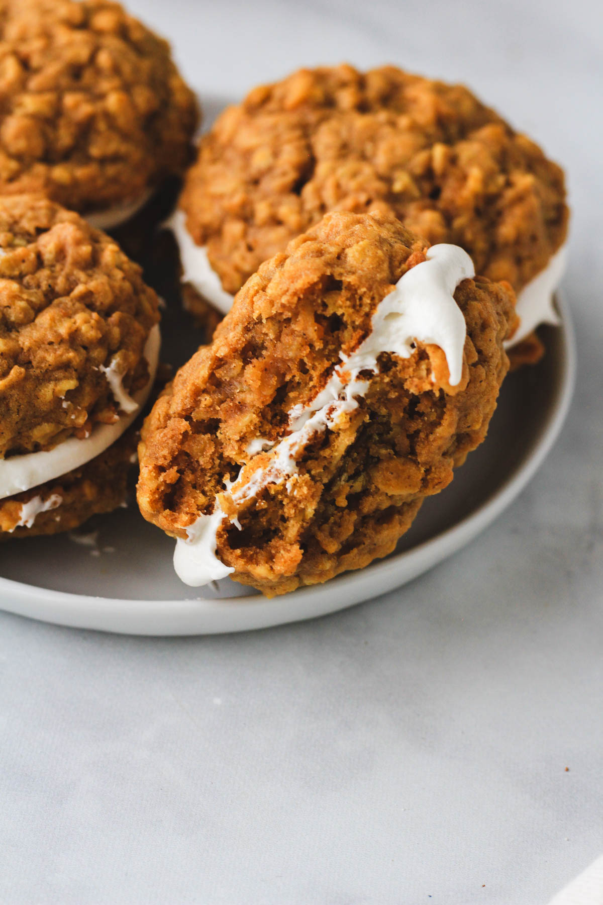 A small white plate with dairy-free pumpkin spice oatmeal cream pie cookies with one on the side and a bite taken out to show the filling.