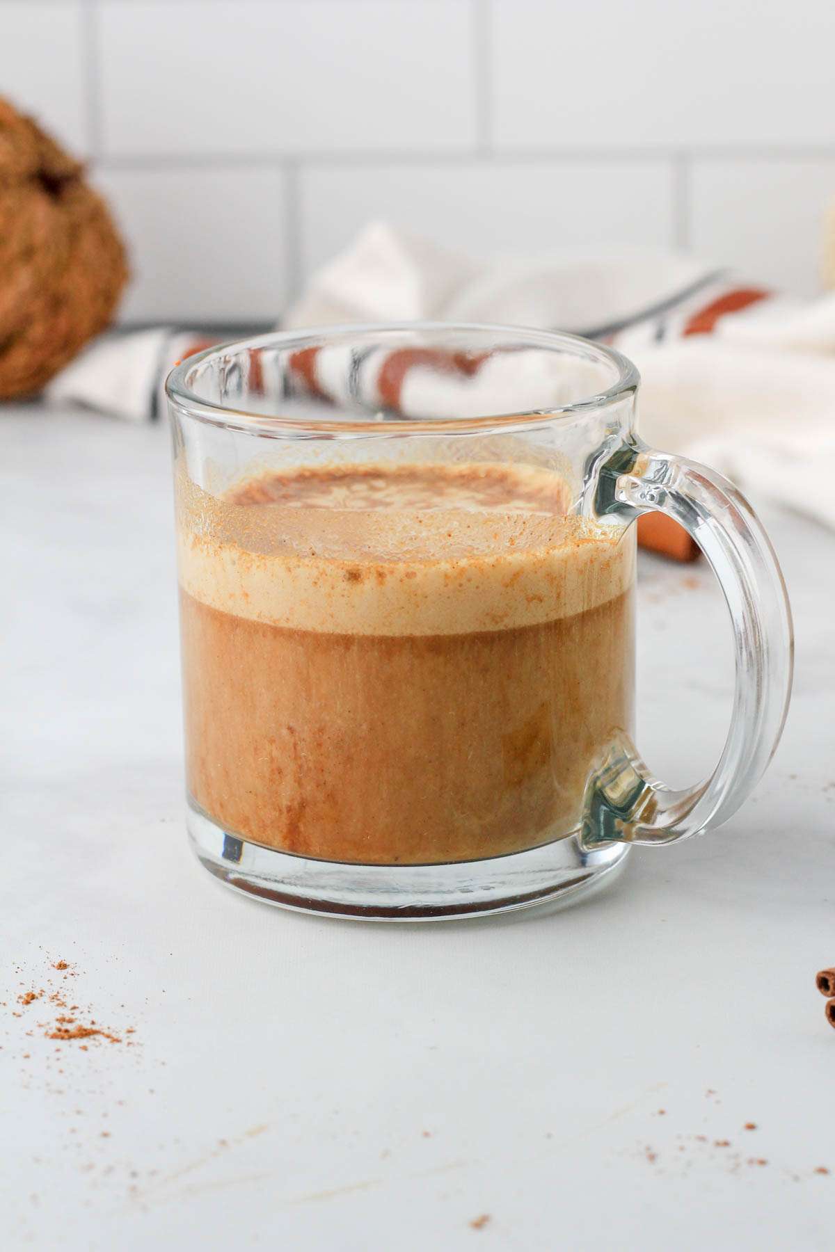 A glass coffee cup with a finished vegan pumpkin spice latte on a white counter.