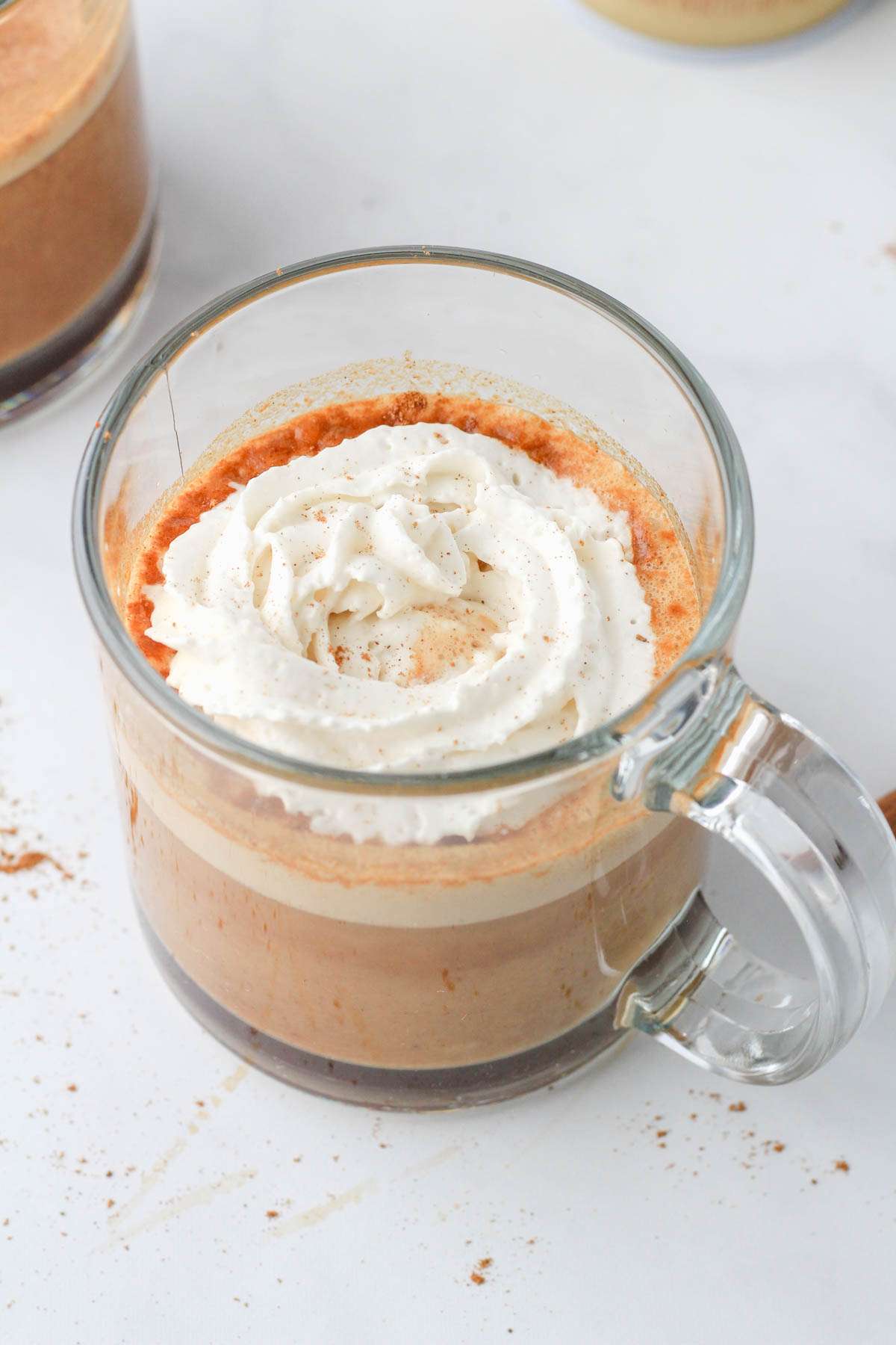 A glass mug with an oat milk pumpkin spice latte topped with vegan whipped topping.