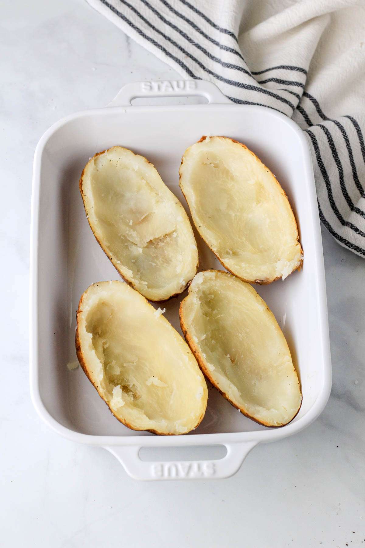 A white baking dish with four halves of baked potato shelled and ready for filling.
