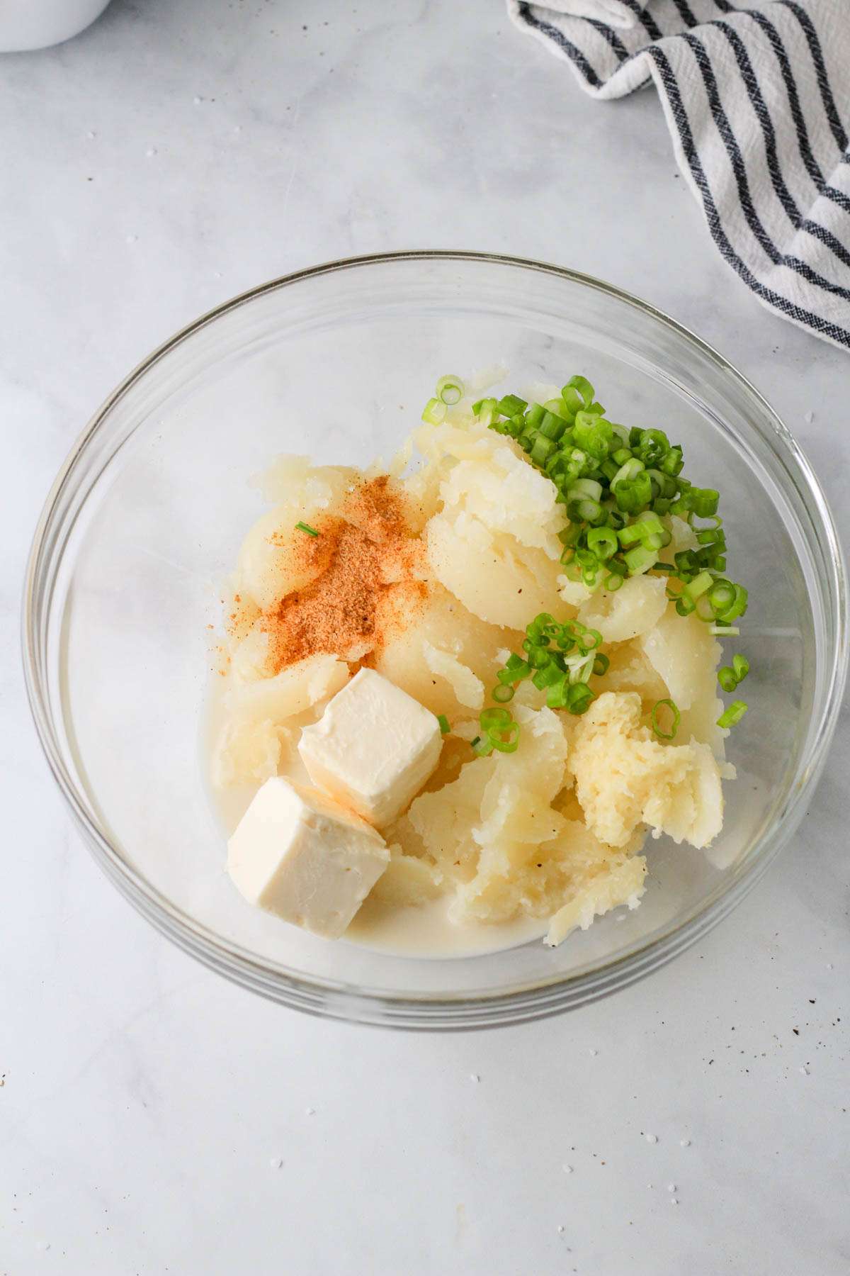 A small glass bowl with the remaining ingredients for vegan twice baked potatoes before mixing together.