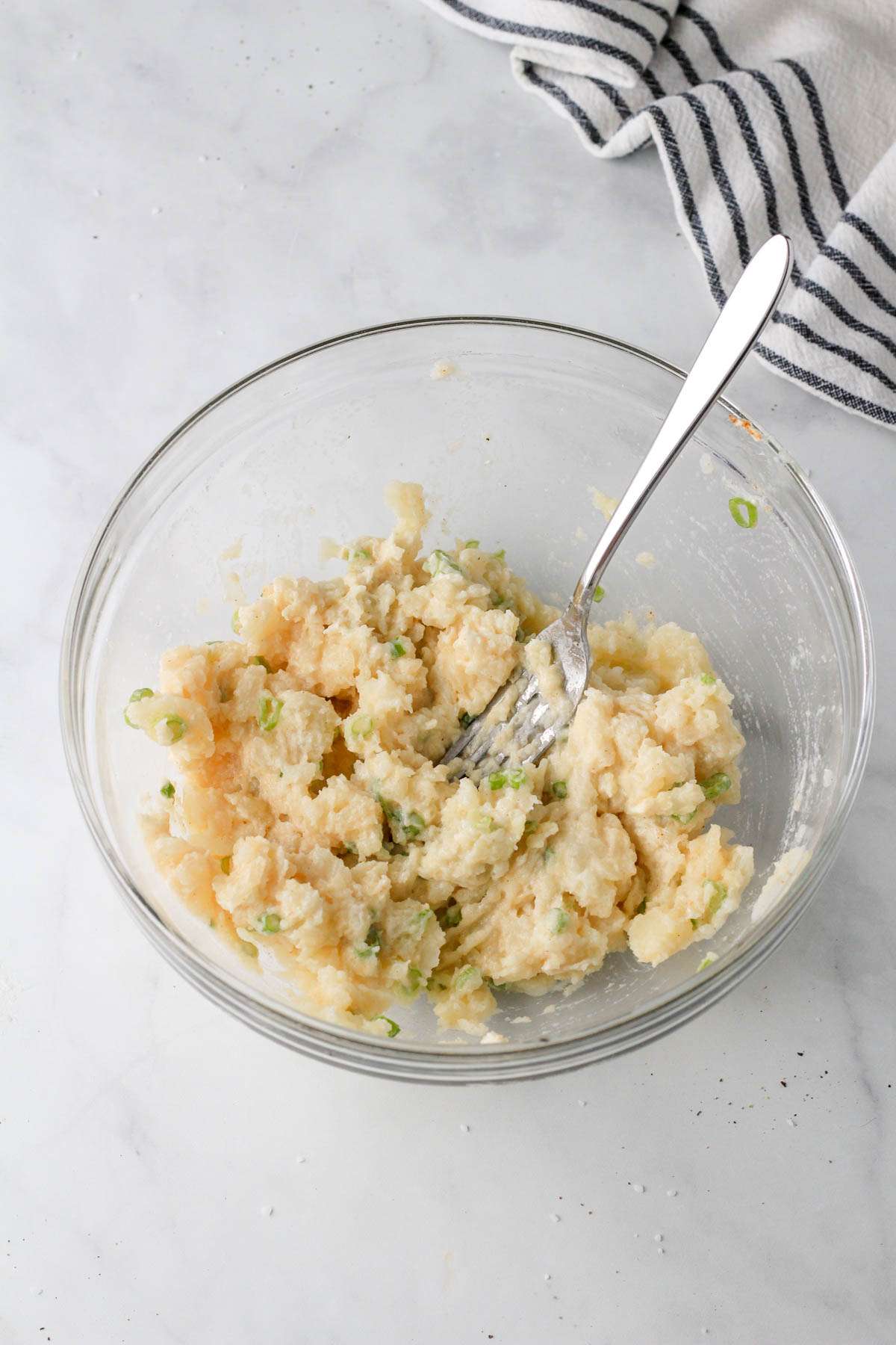 Ingredients for vegan twice baked potato filling mixed together with a silver fork in a glass bowl.
