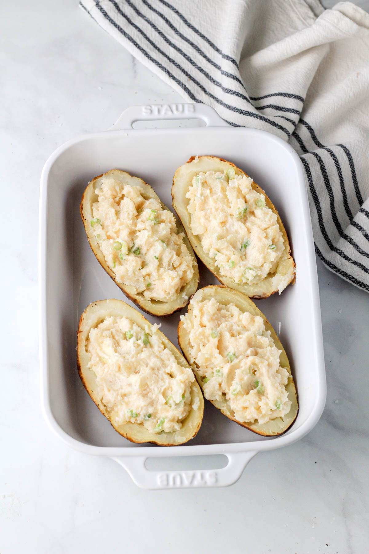 A white baking dish with four halves of baked potatoes filled with the vegan twice baked potato filling before baking.
