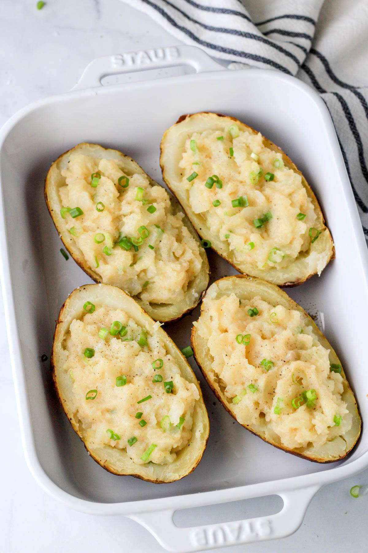 Four vegan twice baked potatoes in a white baking dish after baking.