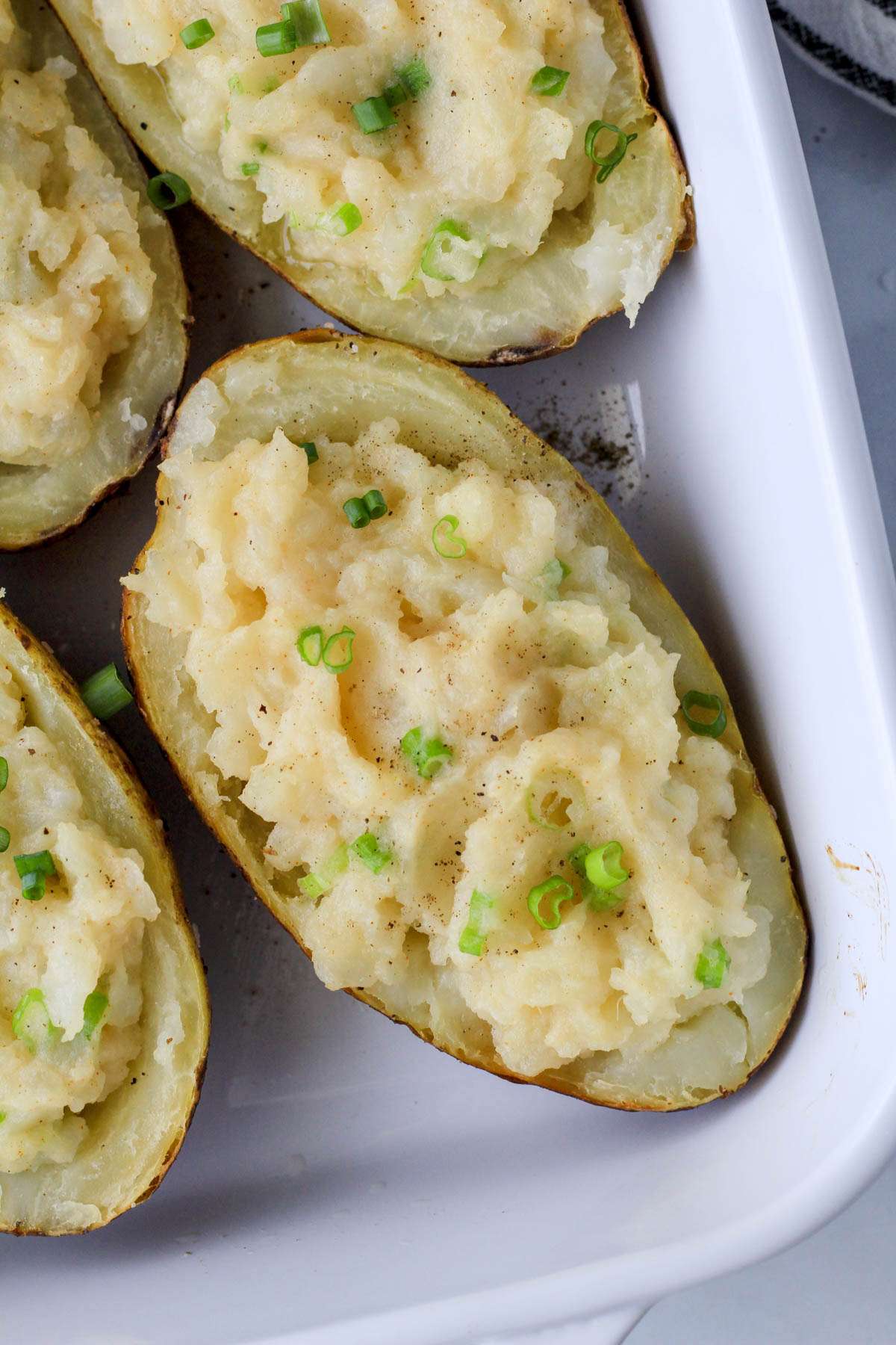 A green onion topped vegan twice baked potato in a white baking dish.