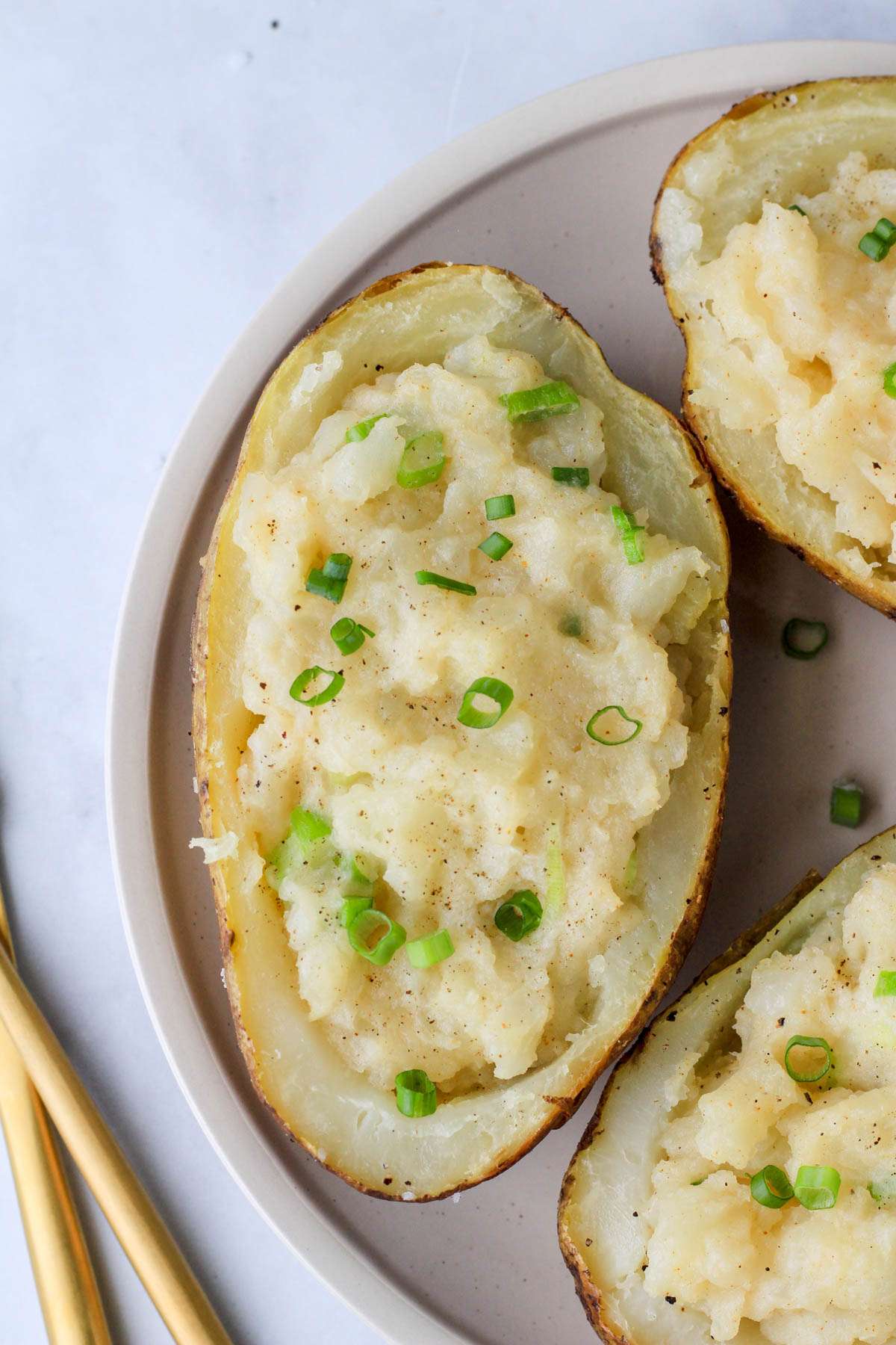 A close up of a loaded vegan twice baked potato topped with green onion on a cream colored plate.