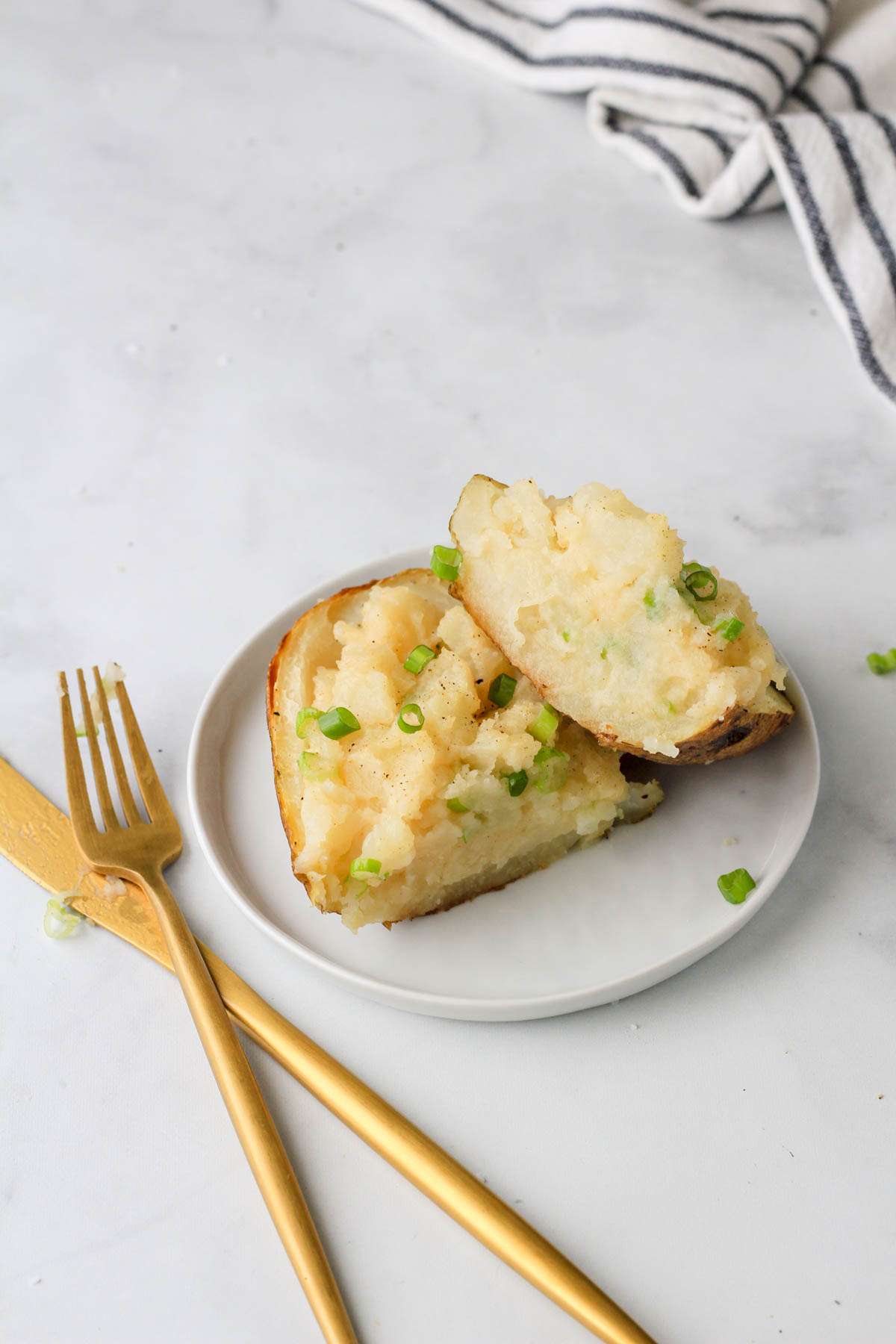 A small with plate with a fork and knife to the left with a sliced vegan twice baked potato on top.