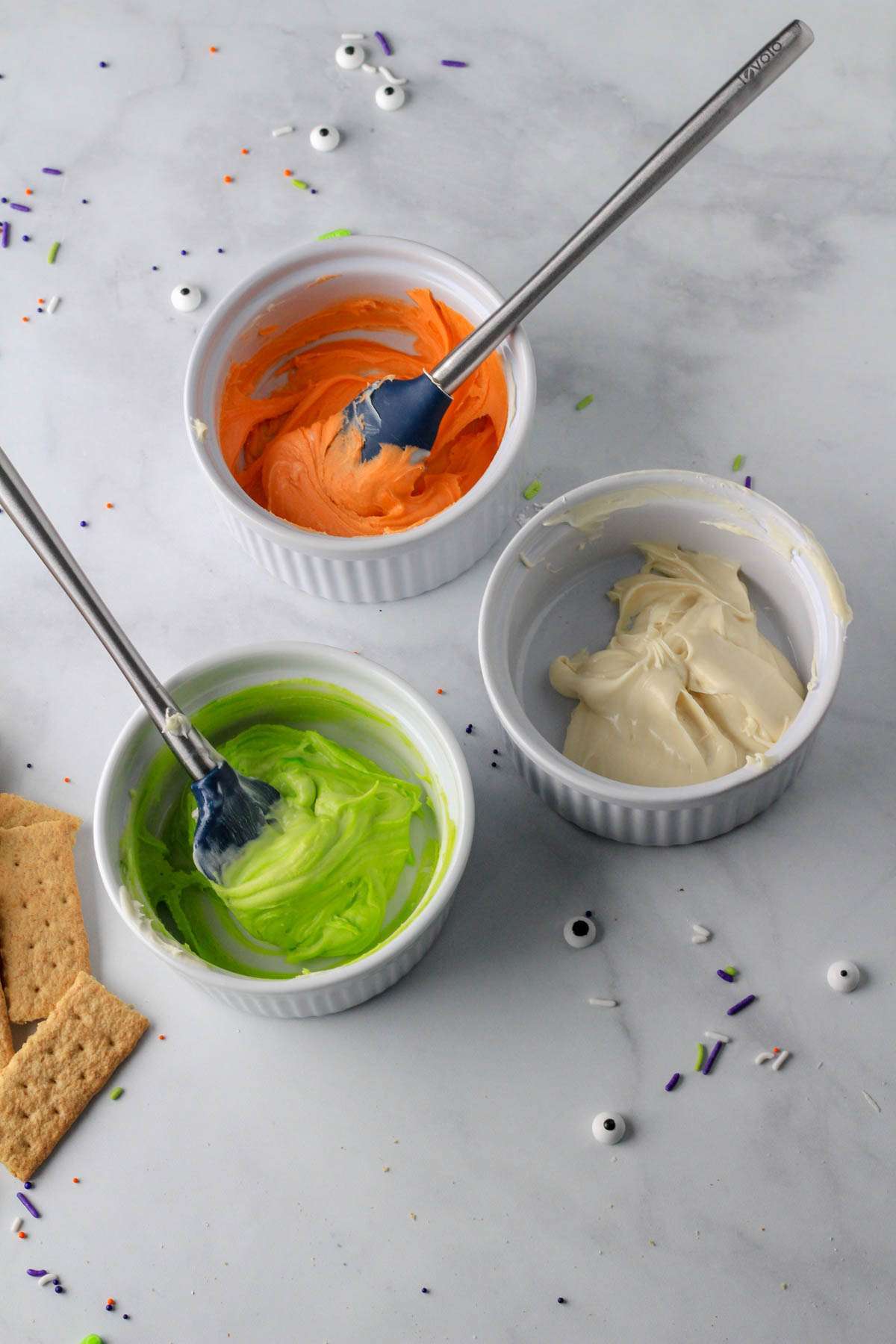 Three white bowls with melted white chocolate colored with orange and green food dye.