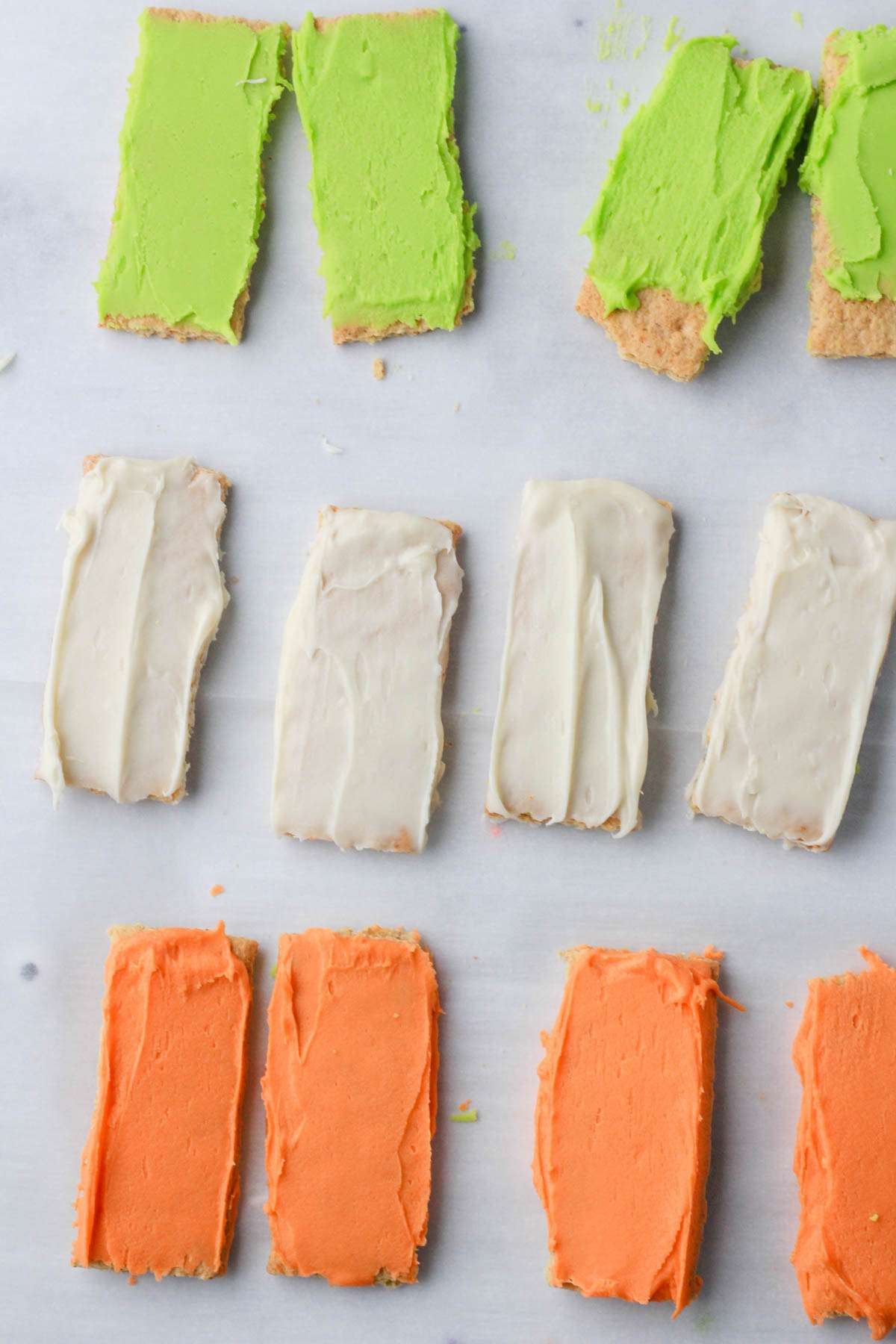 A white counter with graham crackers dipped with green, white, and orange white chocolate.