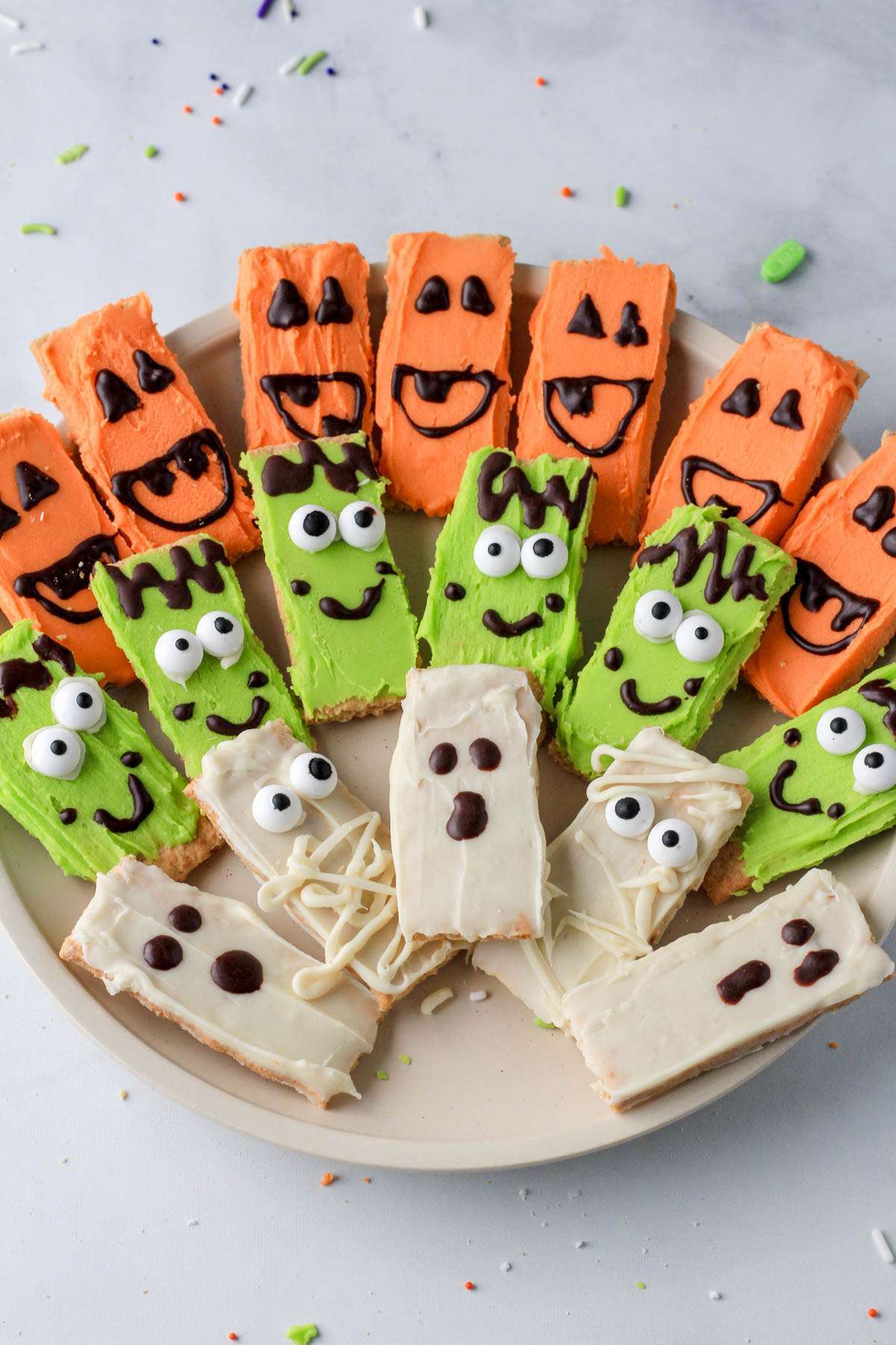 A white plate topped with Halloween white chocolate dipped graham crackers that look like mummies, pumpkins, and monsters.