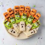 A white plate with rows of pumpkin, monster, and ghost, and mummy decorated graham crackers for Halloween.