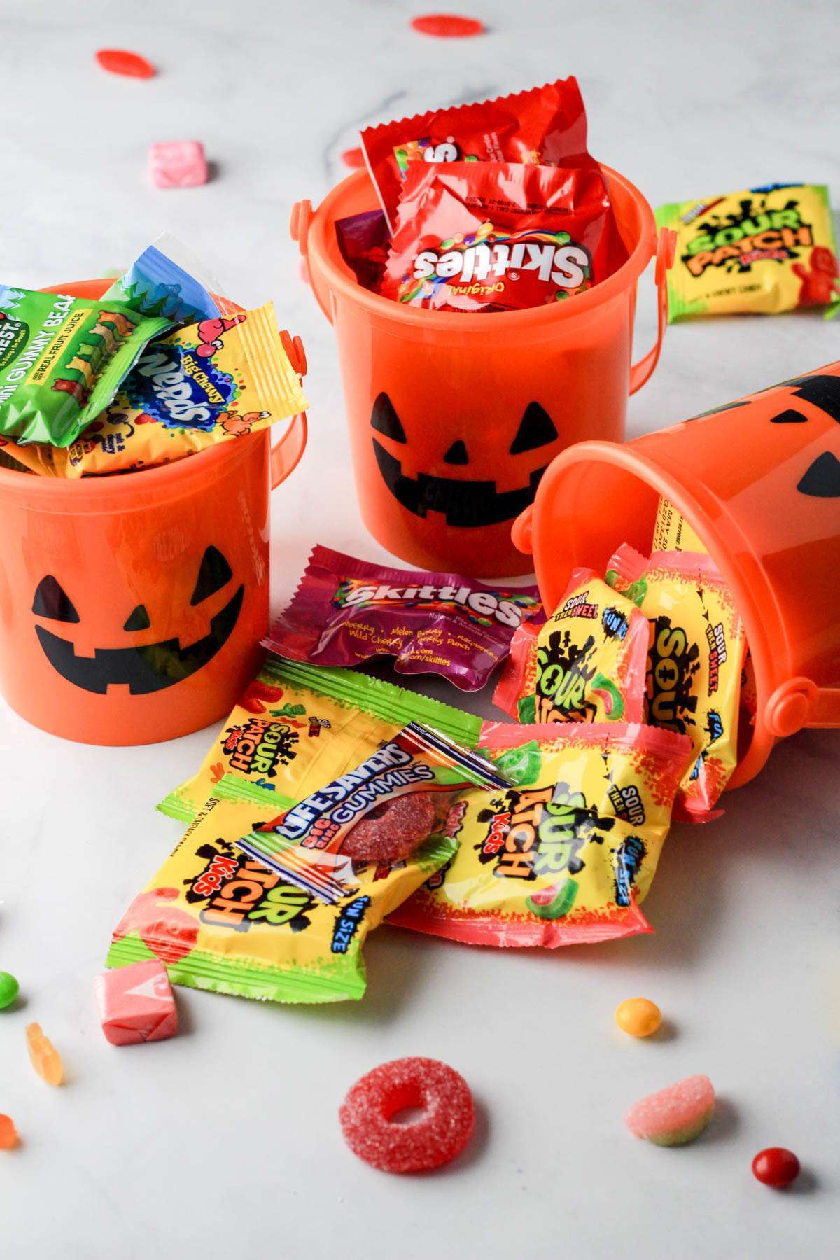 Three small orange jack-o-lantern buckets filled with dairy-free candy for Halloween.