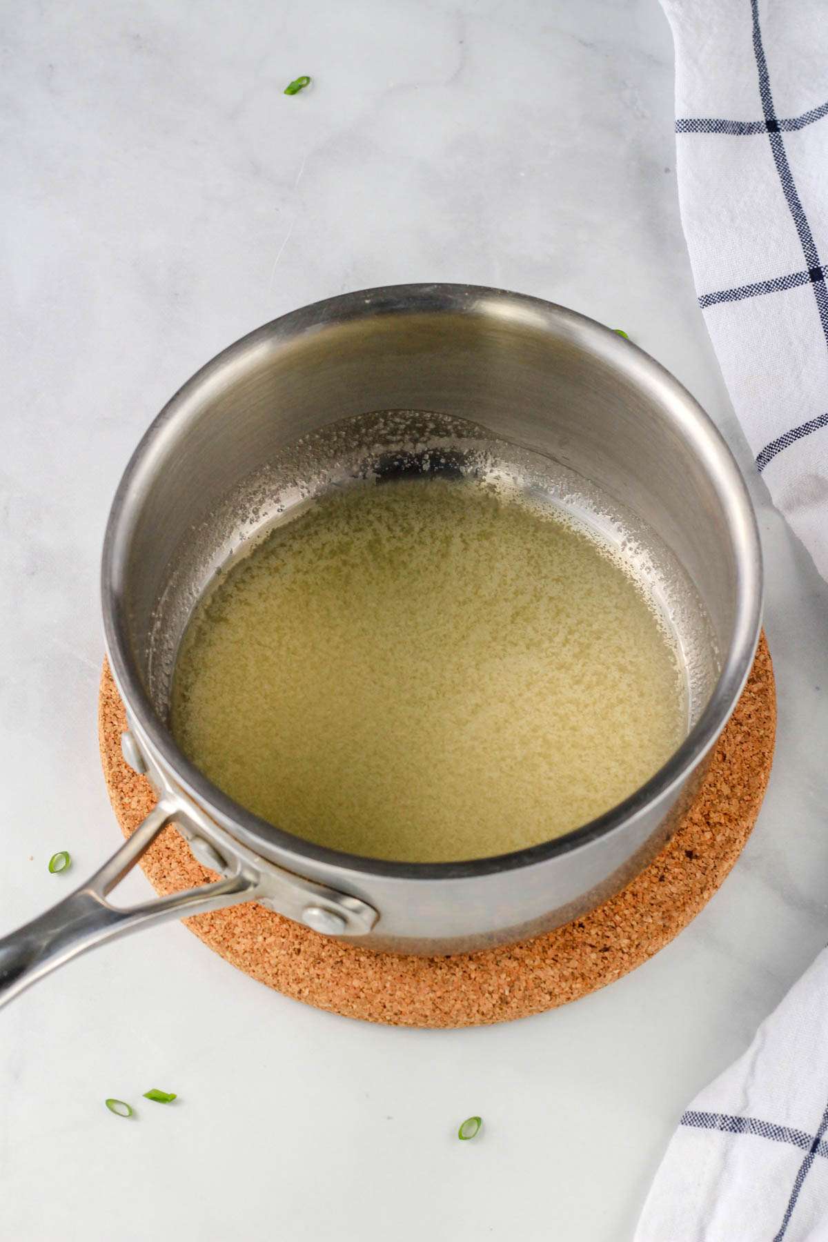 A silver saucepan with melted vegan butter on a cork trivet.