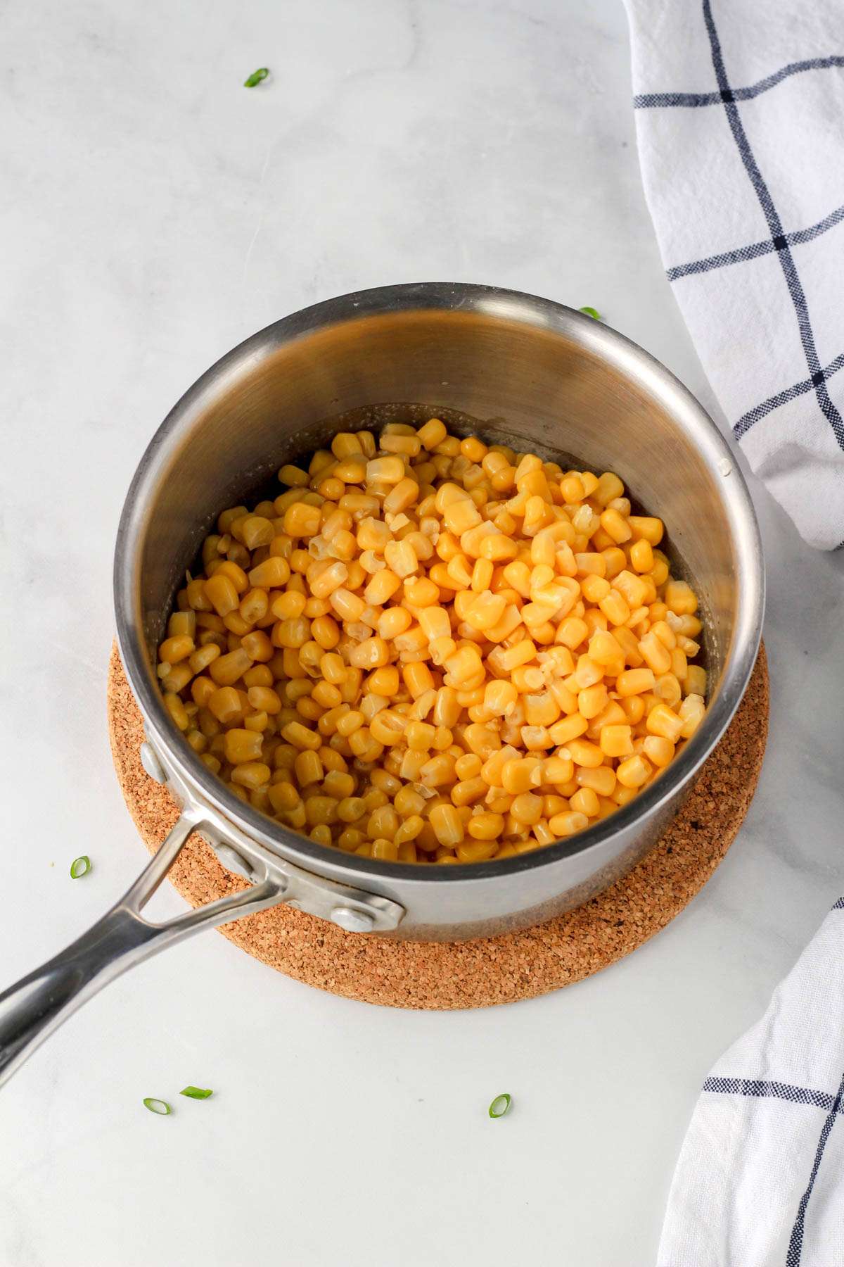 A sauce pan with corn on a cork trivet.