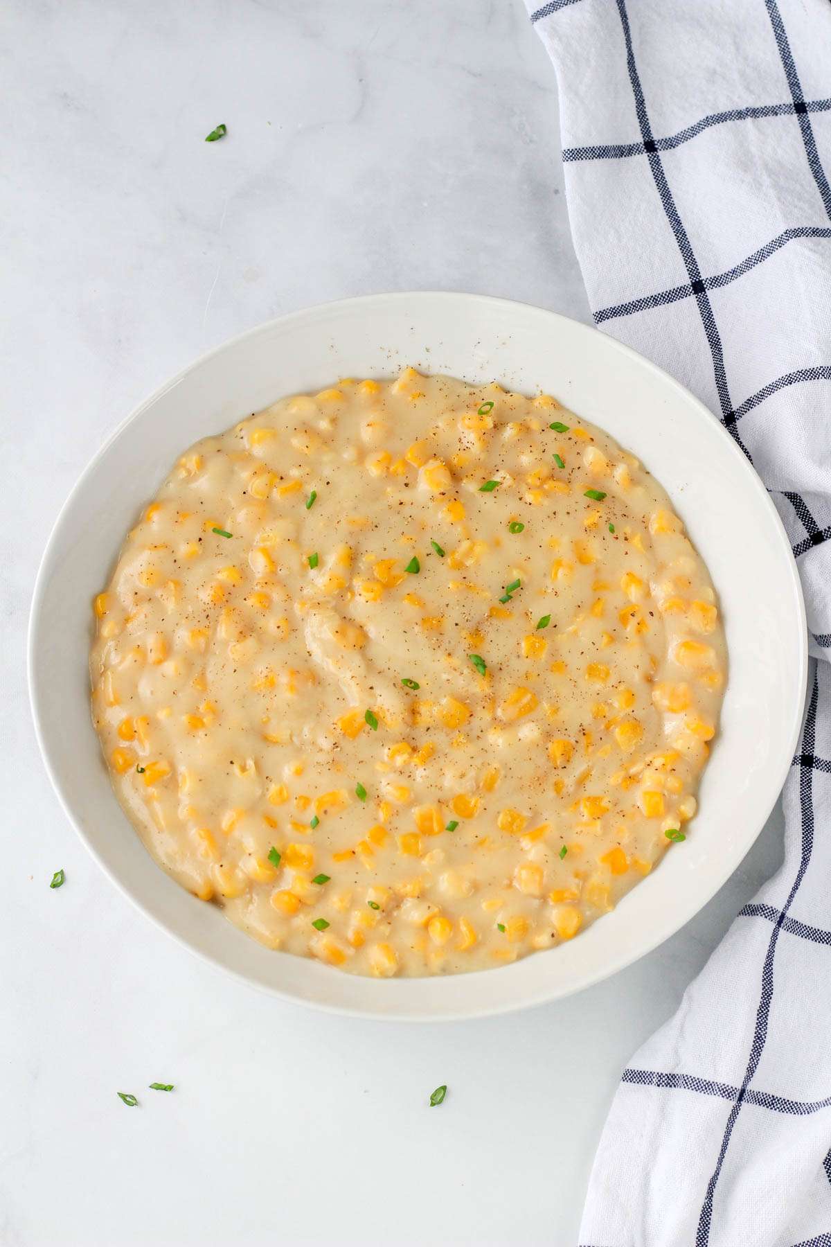 A white bowl filled with dairy-free creamed corn topped with green onion.