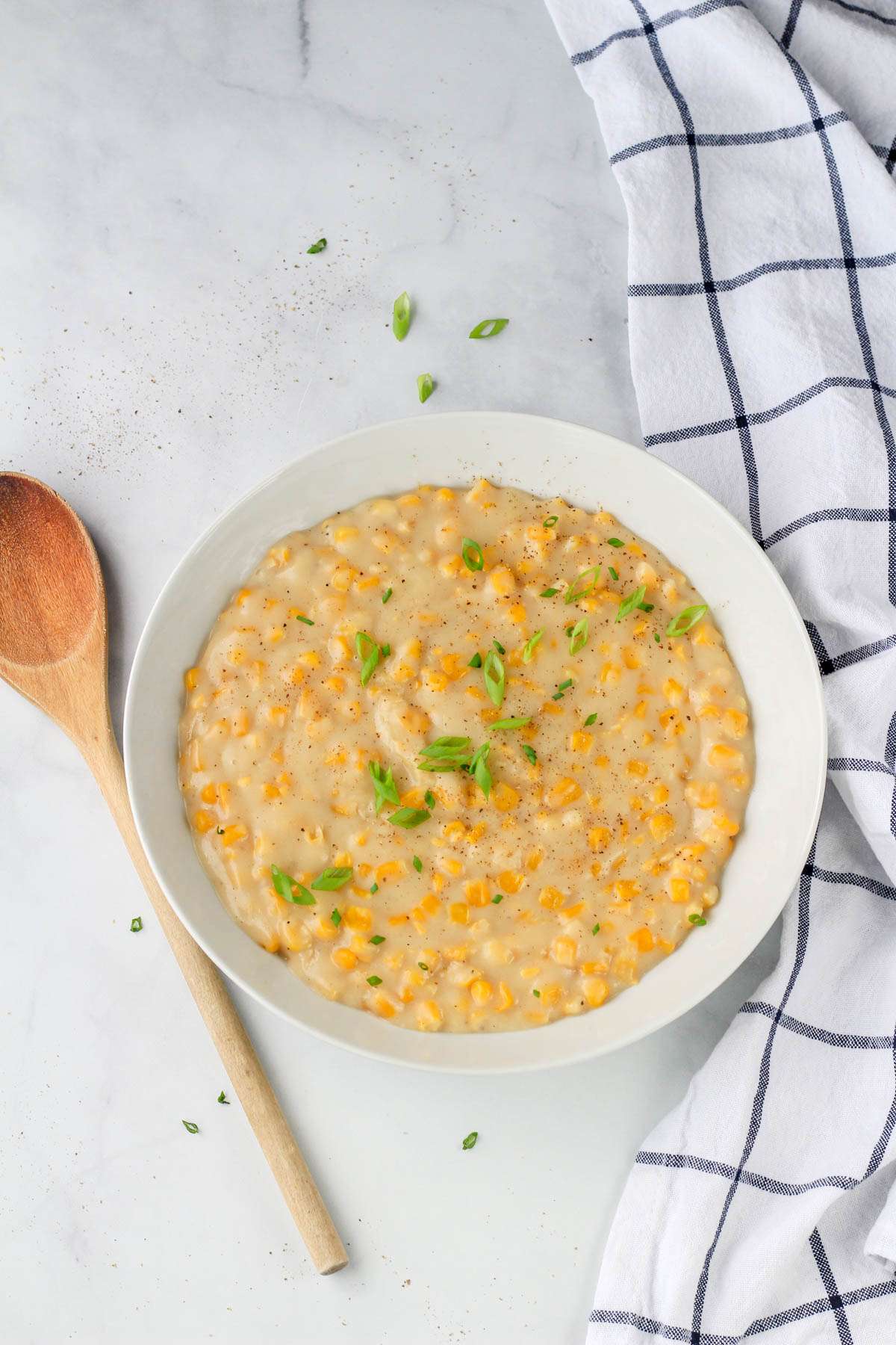 A bowl of dairy-free creamed corn on a white counter with a wooden spoon to the left.