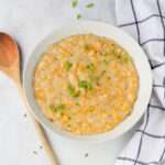 A white bowl of vegan creamed corn topped with green onion with a wooden spoon to the left.
