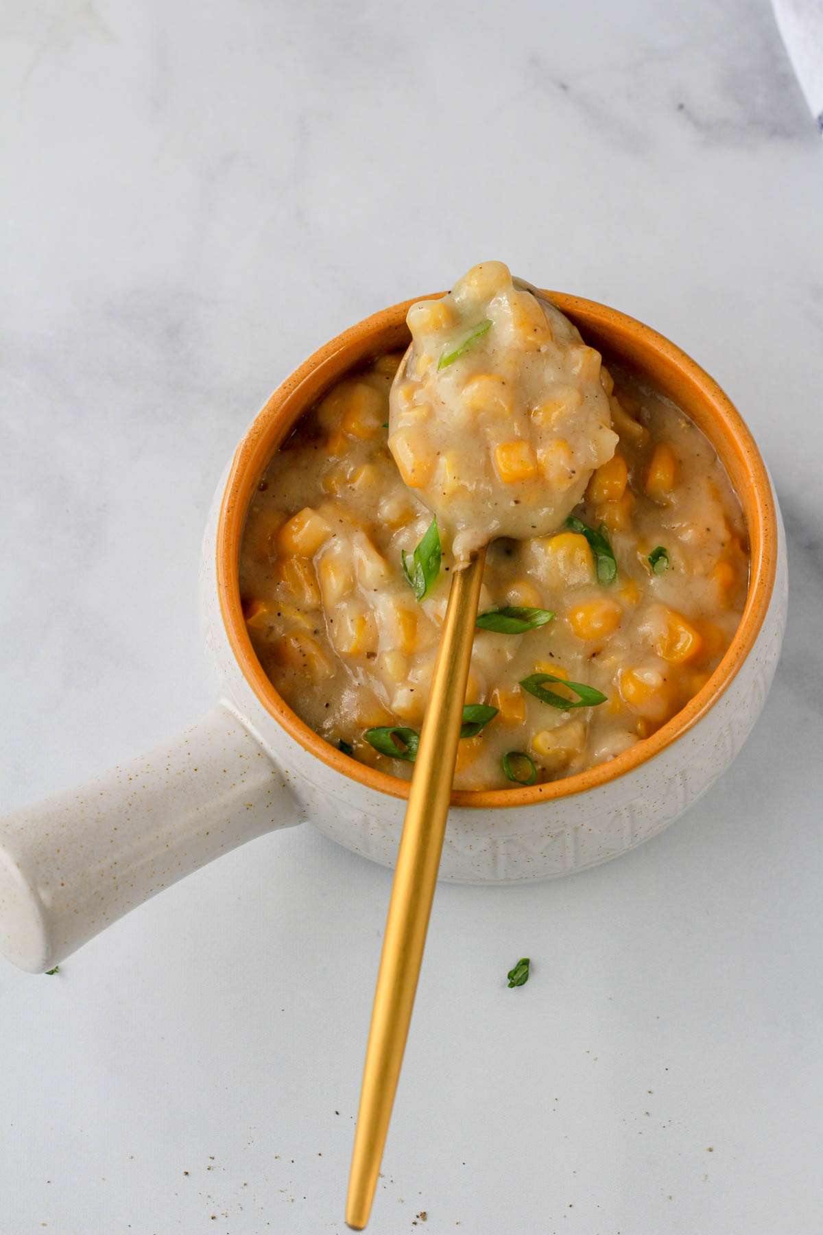 A gold spoon on top of a white and orange bowl of vegan creamed corn.