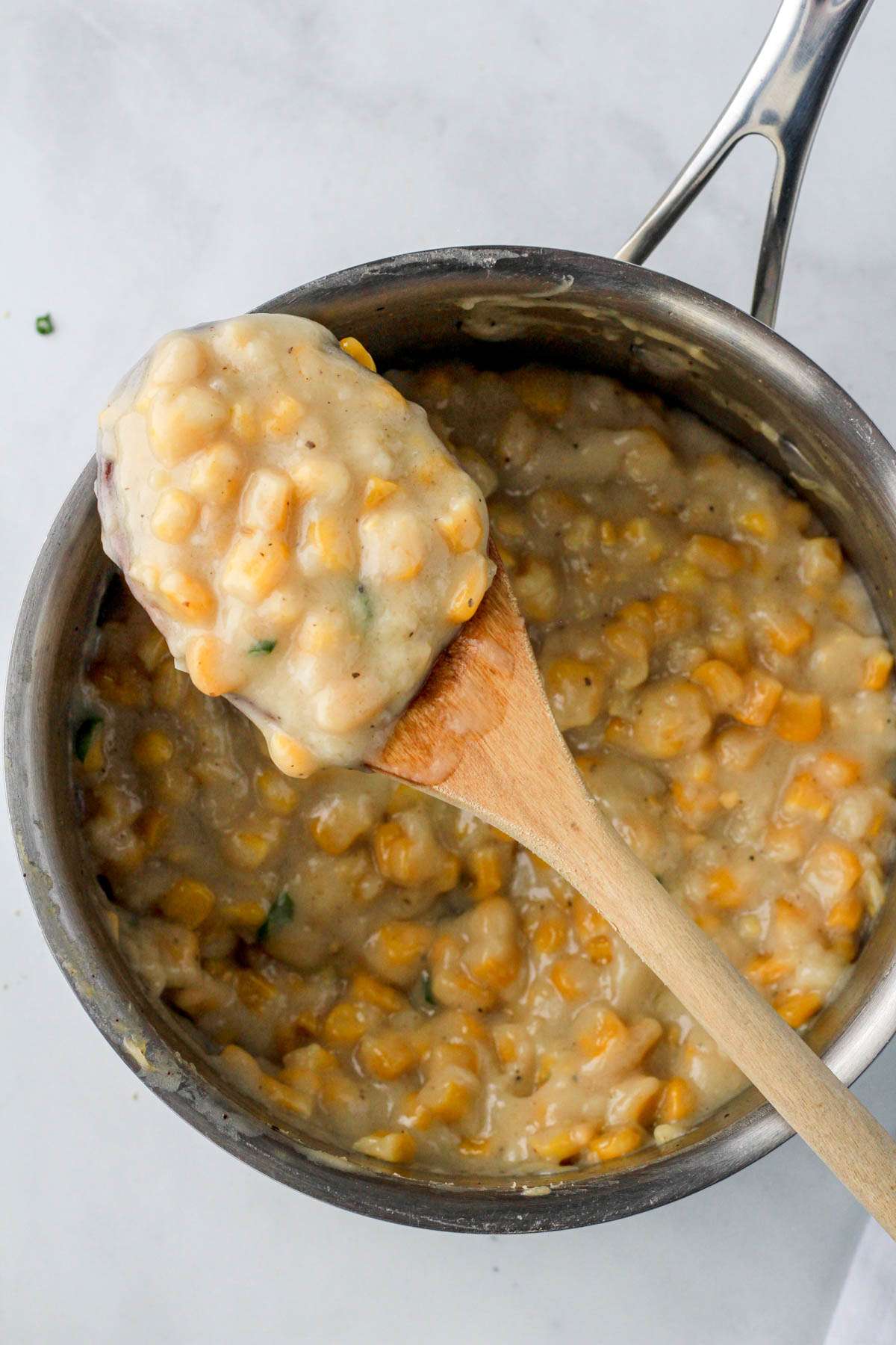 A wooden spoon on top of a sauce pan with vegan creamed corn.