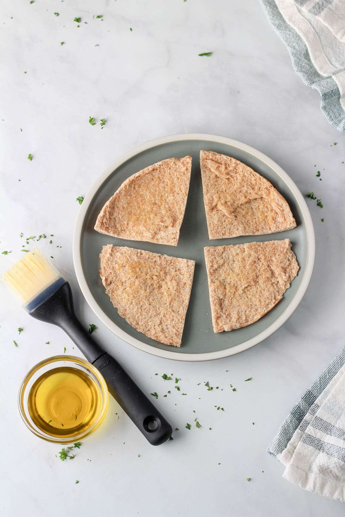 A green plate topped with slices of pita bread with a small bowl of olive oil and a pastry brush to the left.