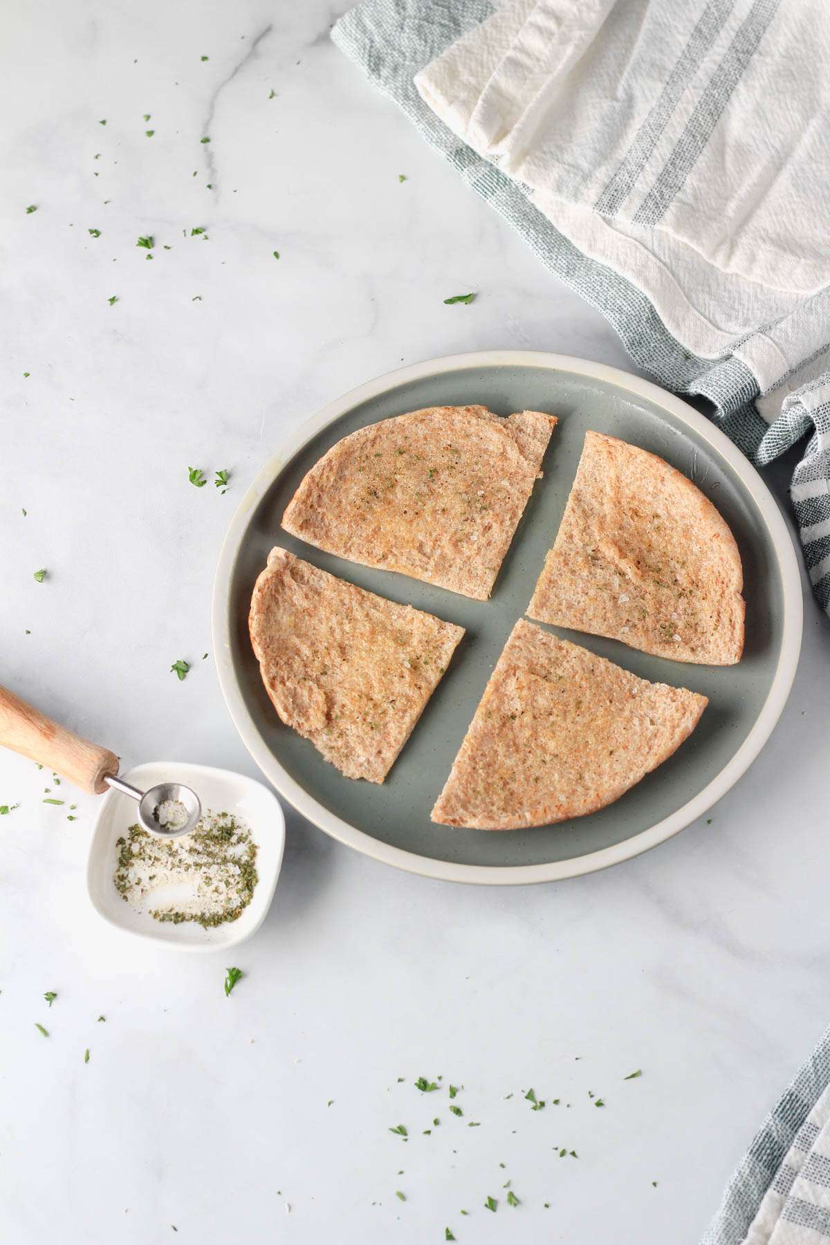 A small green plate with oil brushed slices of pita bread sprinkled with a seasoning blend.