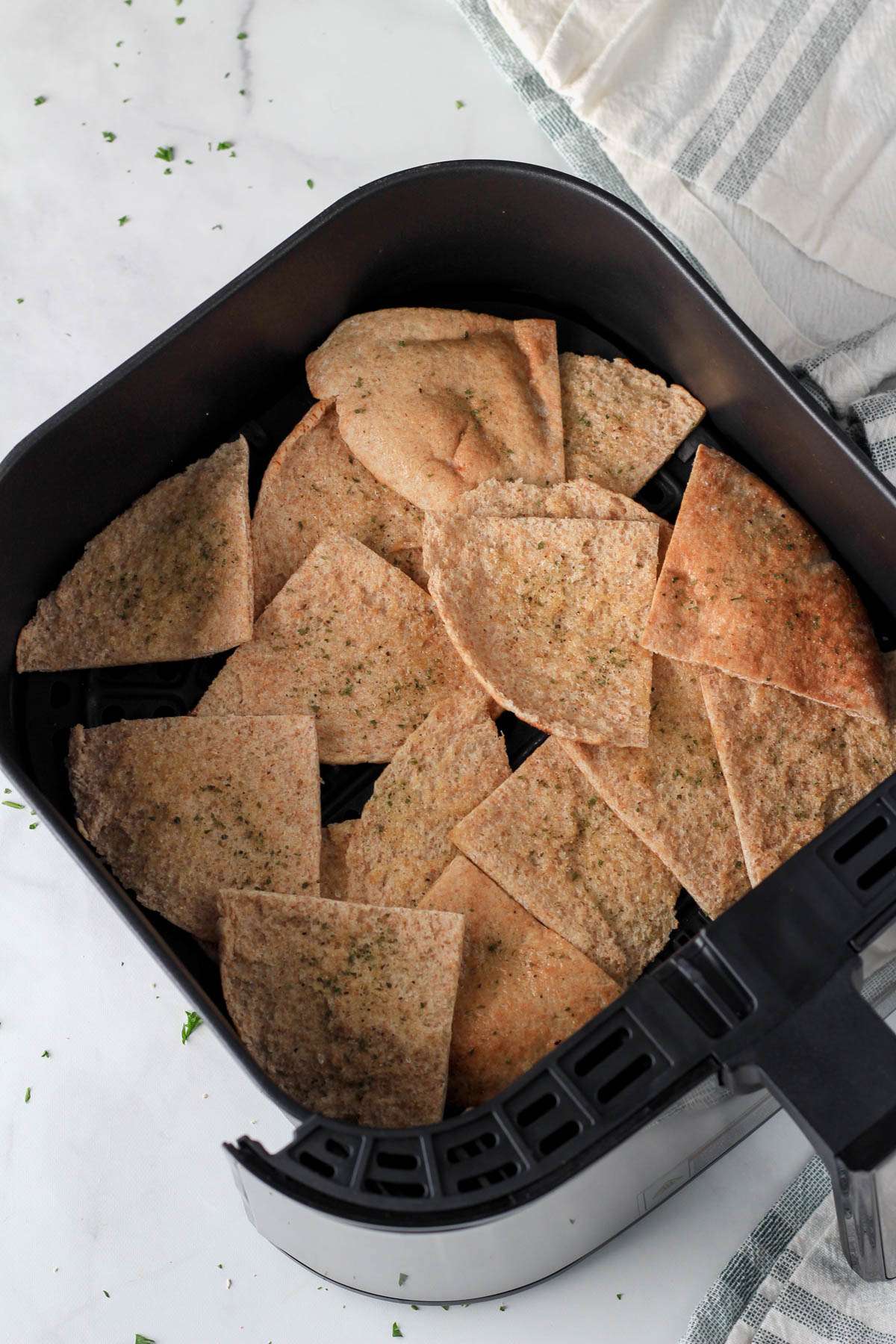 An air fryer basket with pita bread pieces scattered in before cooking.