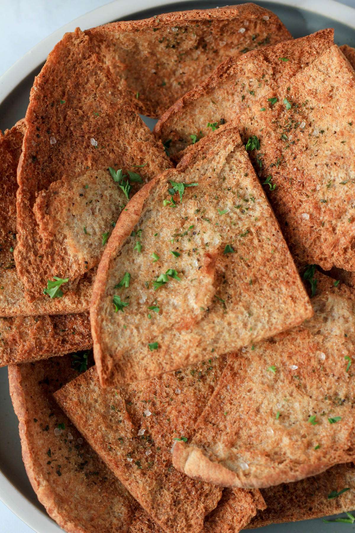 A close up of a pile of vegan air fryer pita chips sprinkled with parsley.