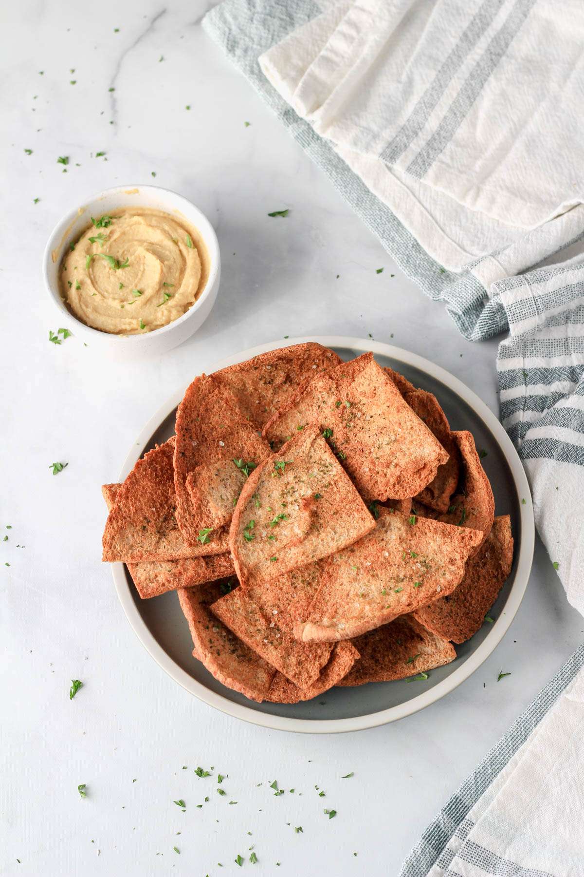 A small green plate with a pile of air fryer pita chips and a small bowl of hummus in the top left corner.