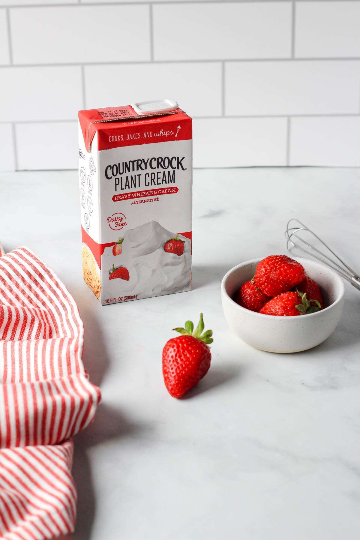 A white counter with a white backsplash and a container of Country crock plant cream on the counter with red strawberries.