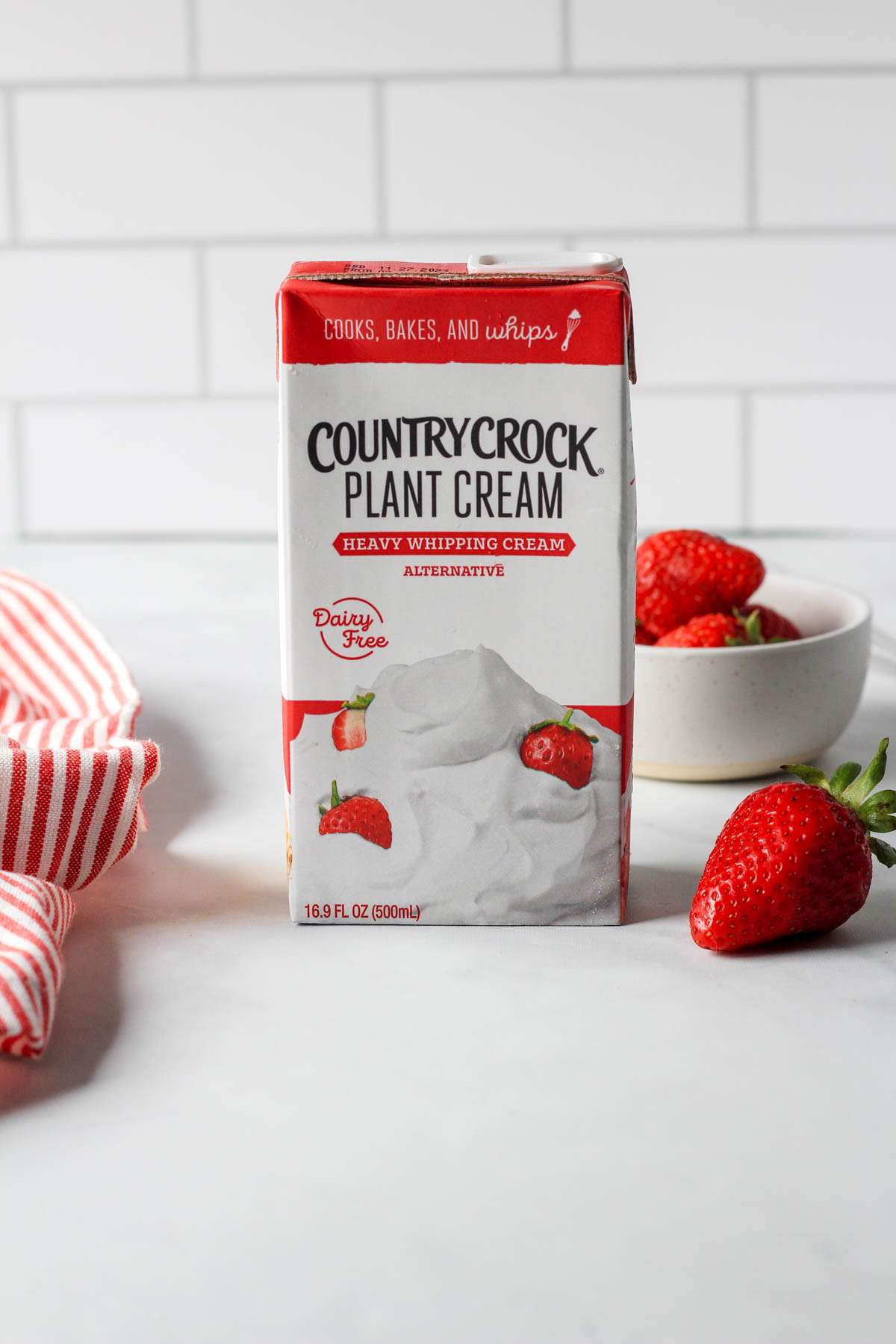 A white and red container of country crock plant cream on a white counter with a red strawberry on the right.