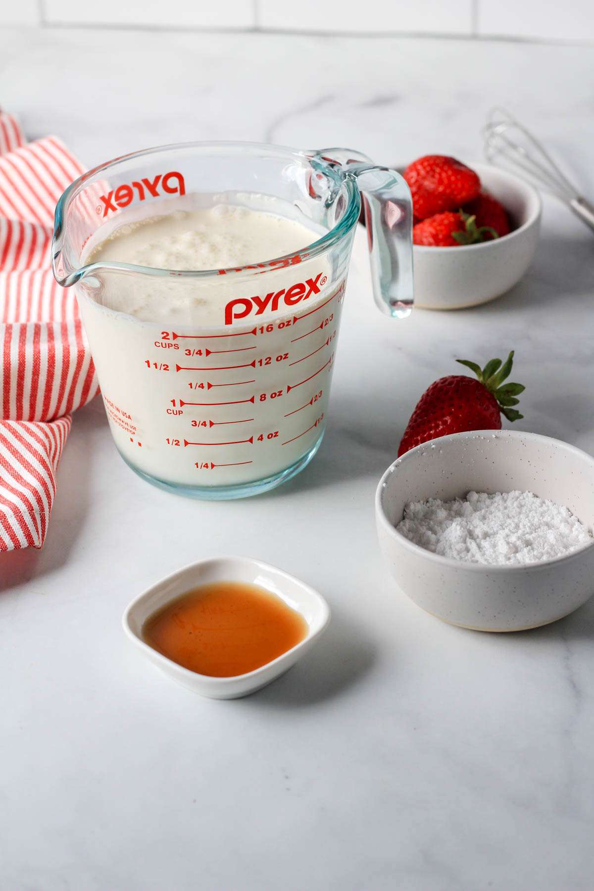 A liquid measuring cup with country crock plant cream a small bowl with powdered sugar and a dish with vanilla in the front.