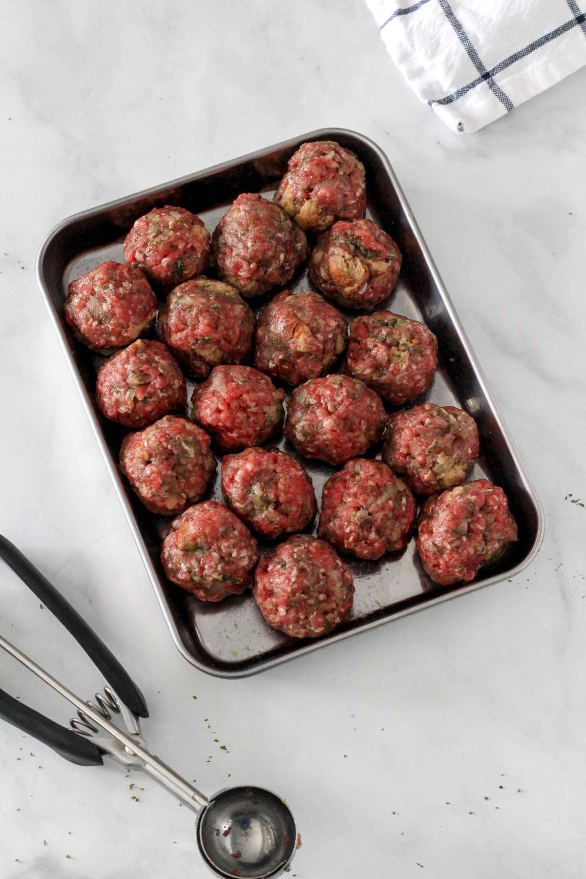 A metal tray with sixteen scooped dairy-free meatballs before cooking.