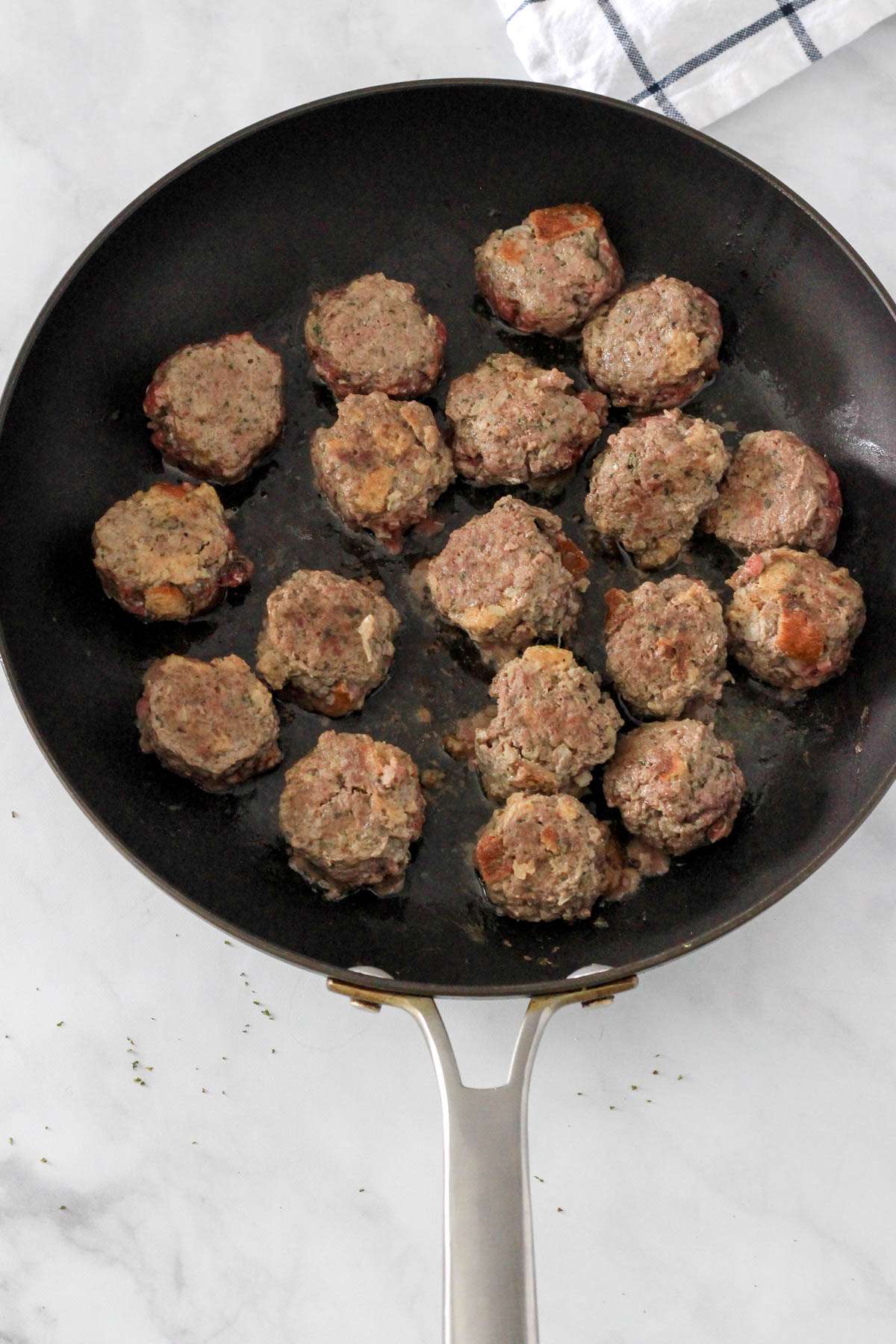 A non-stick skillet with dairy-free meatballs after cooking halfway.