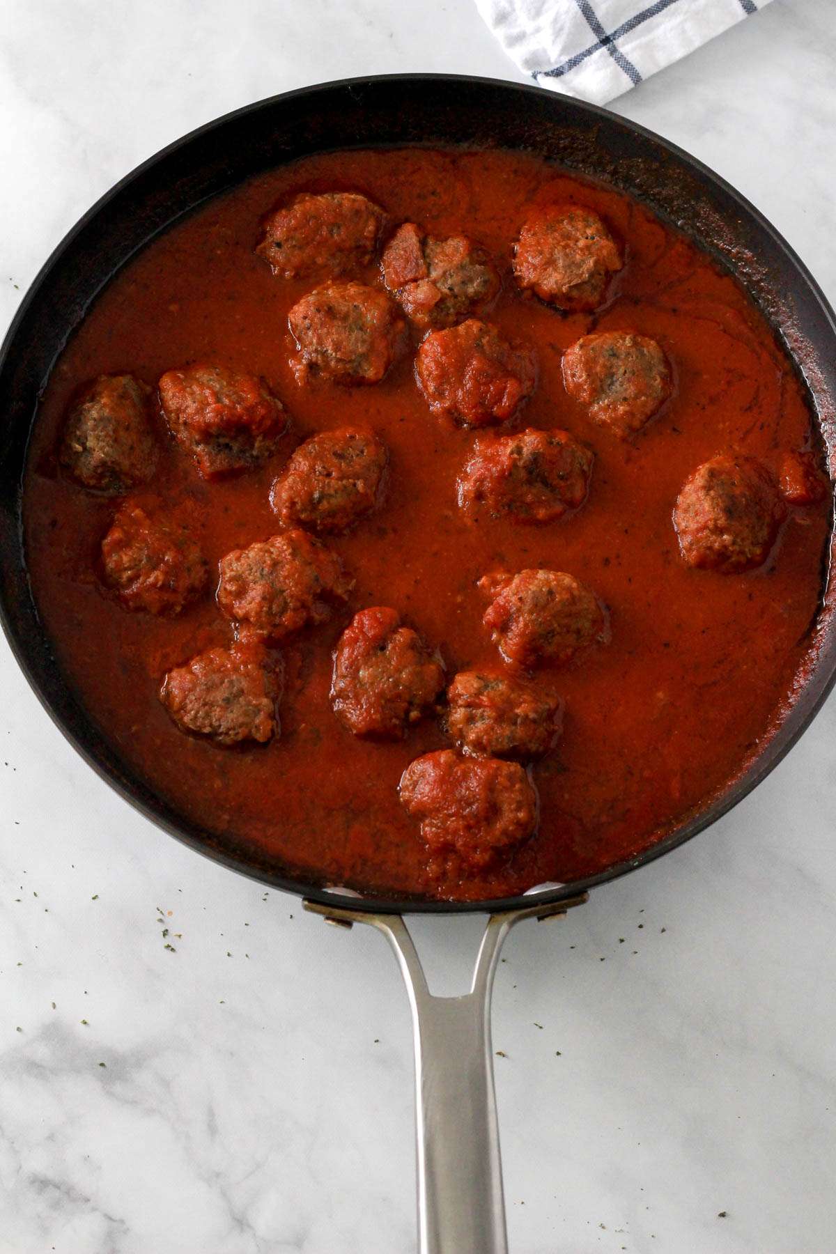 A non-stick skillet with dairy-free meatballs cooking in red sauce.