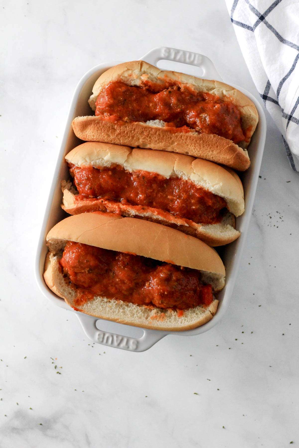 Three meatball subs in a white baking dish before baking.