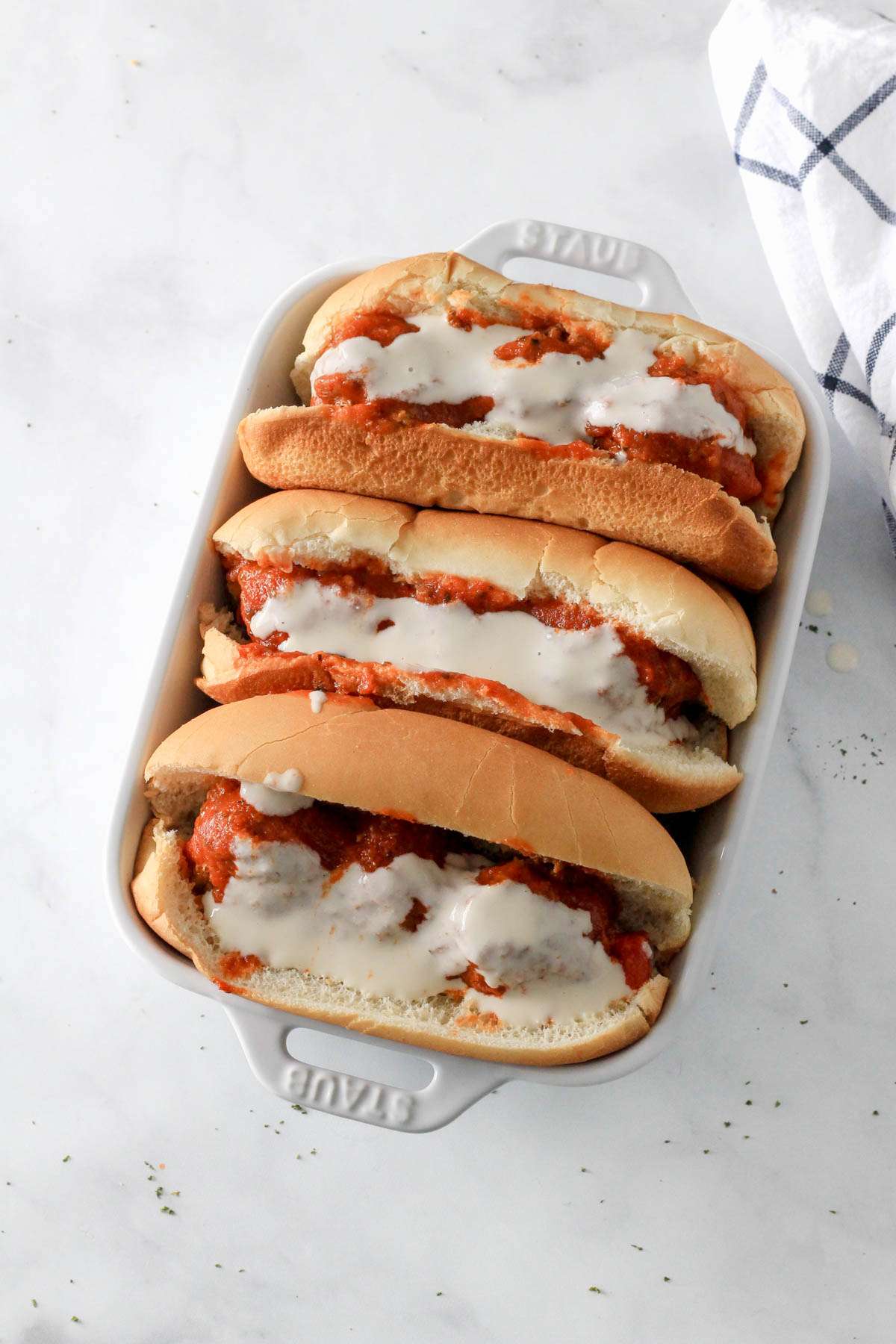 Three dairy-free meatball subs topped with a vegan cheese before baking on meatballs.