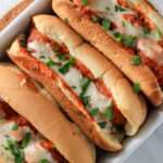 A close up of baked dairy-free meatball subs with parsley.