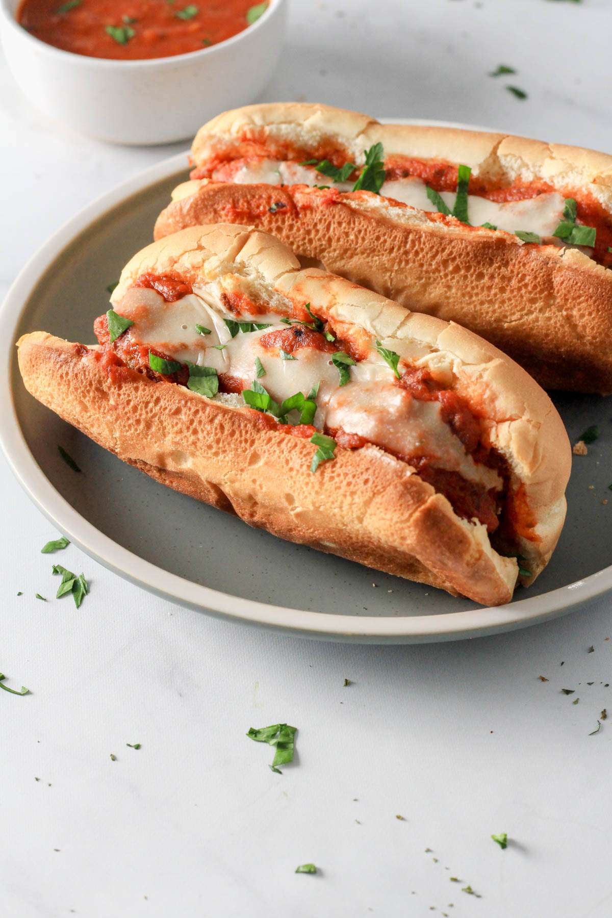 A dairy-free meatball sub from the side on a green and white plate with another dairy-free meatball sub sandwich behind it.
