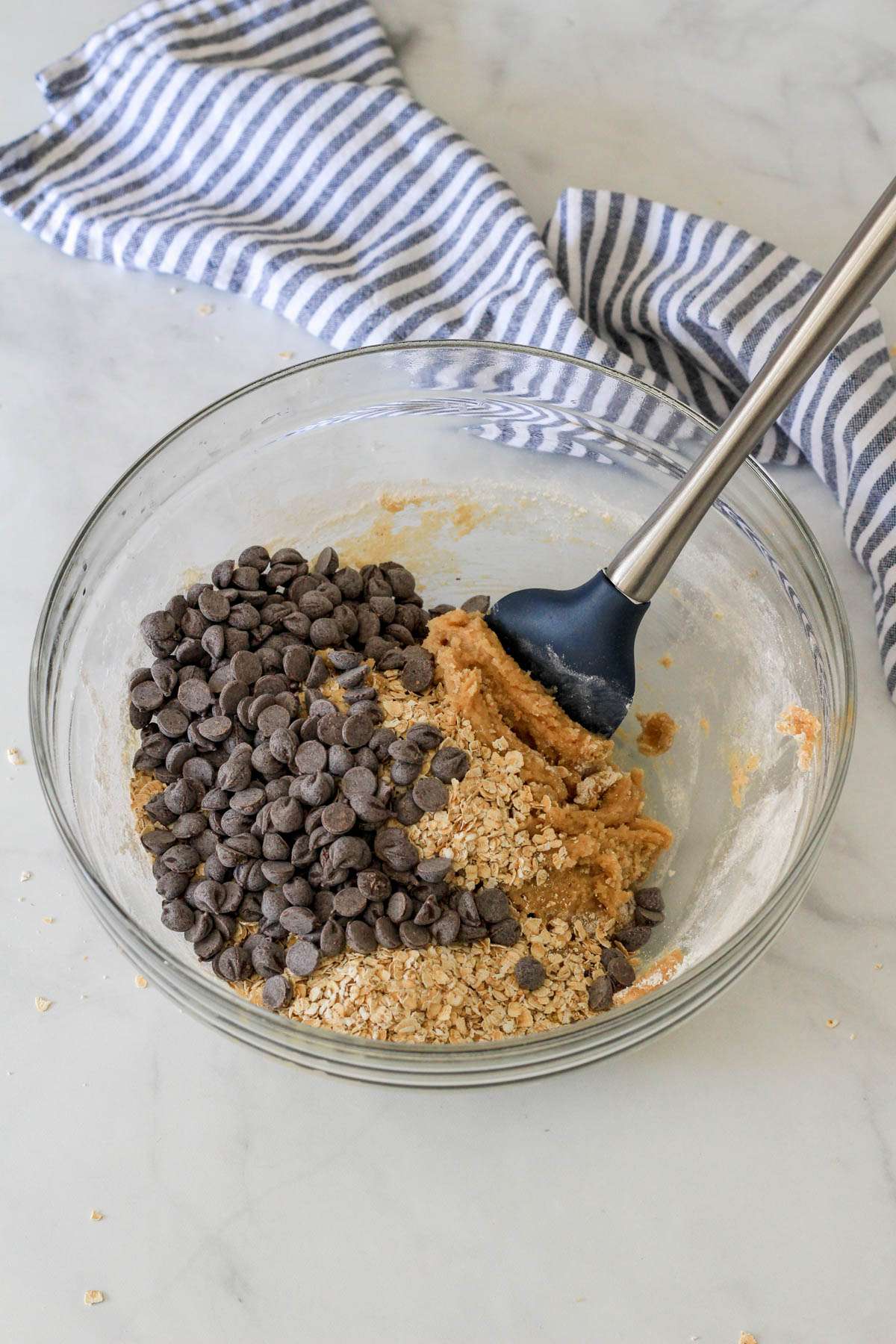 A glass mixing bowl with oatmeal chocolate chip cookie bars dough topped with oatmeal and dairy-free chocolate chips before mixing.