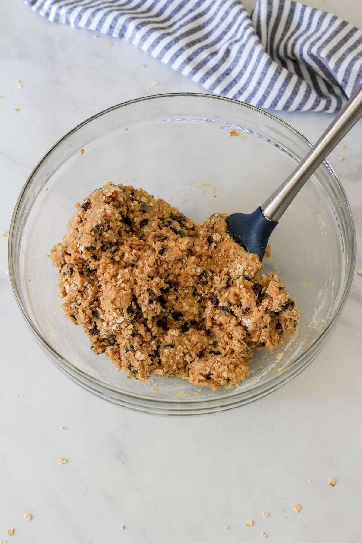 Dairy-Free Oatmeal Chocolate Chip Cookie bars in a glass bowl with a blue and silver spatula after mixing together.